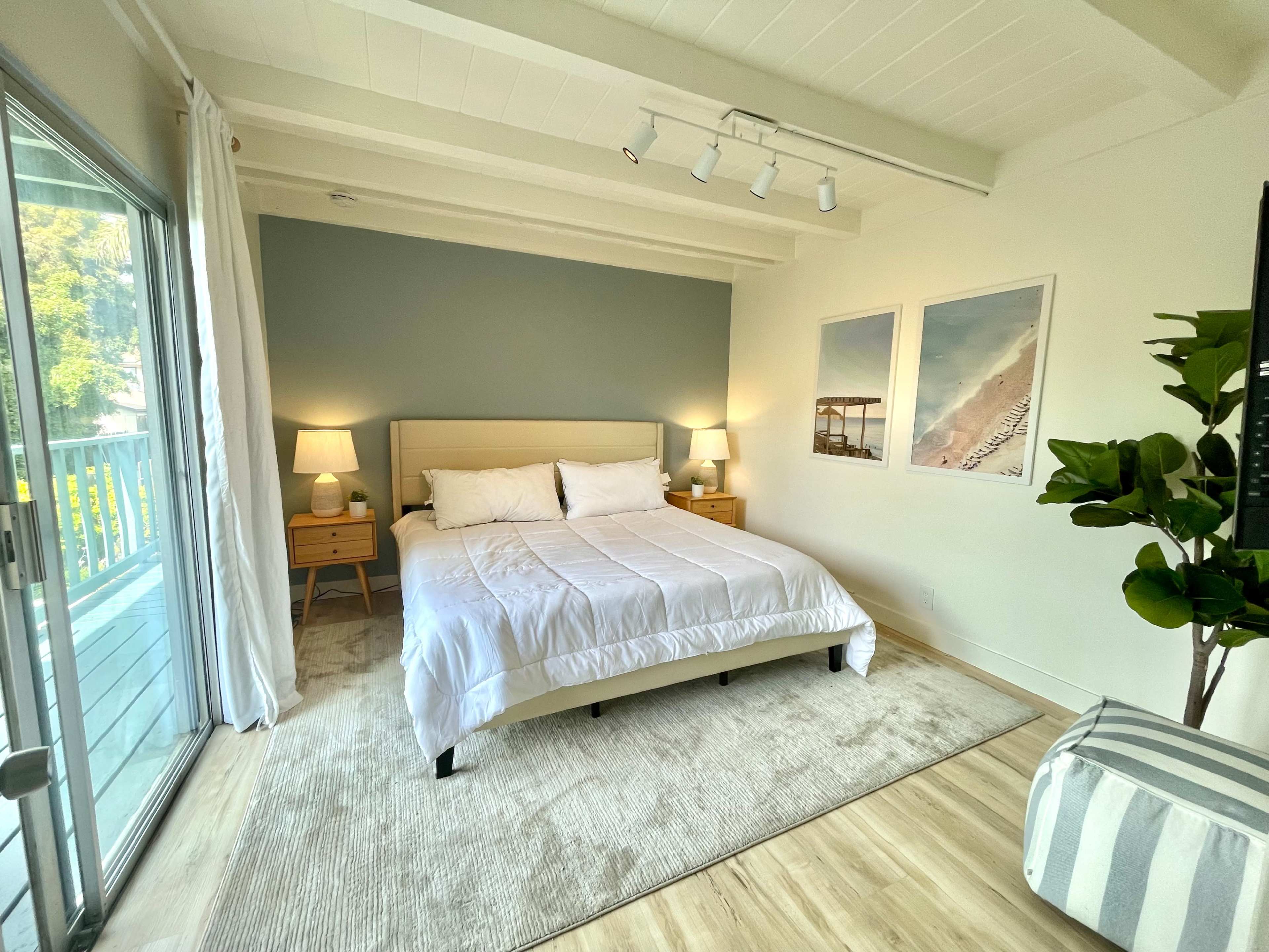 A well-lit bedroom featuring a bed with white linens, two bedside tables with lamps, and large windows opening to a view of nature.