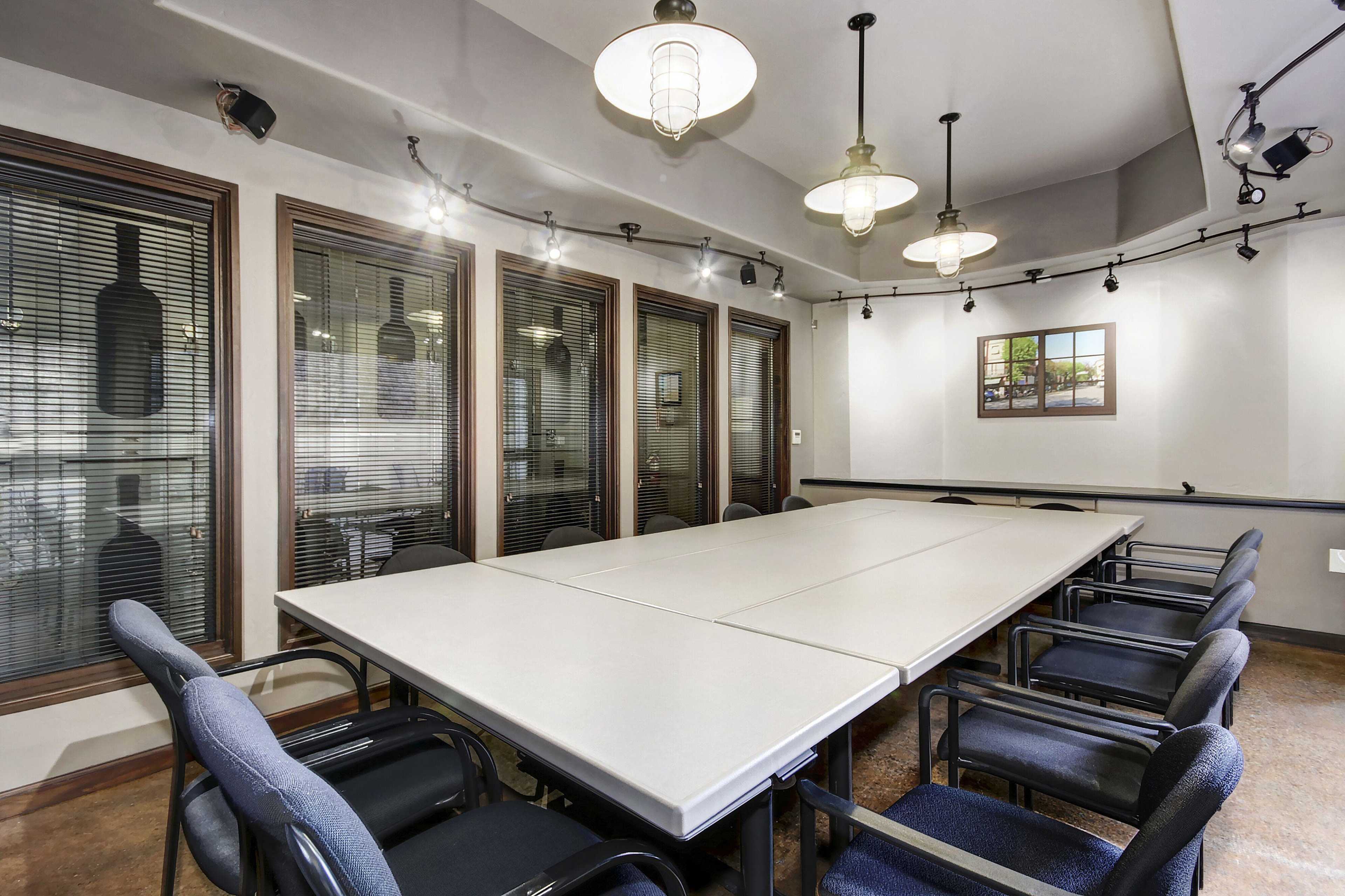 A large conference room features a long rectangular table surrounded by black chairs, with windows and pendant lights adding to the atmosphere.