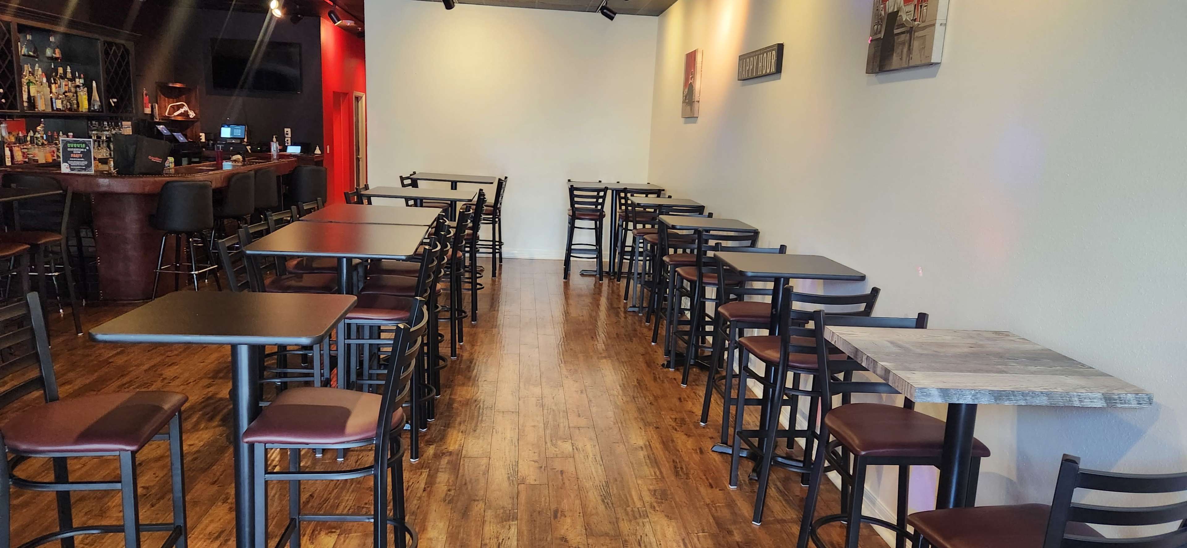 The image shows a spacious dining area with wooden floors, empty tables and chairs arranged neatly, and a bar area visible in the background.