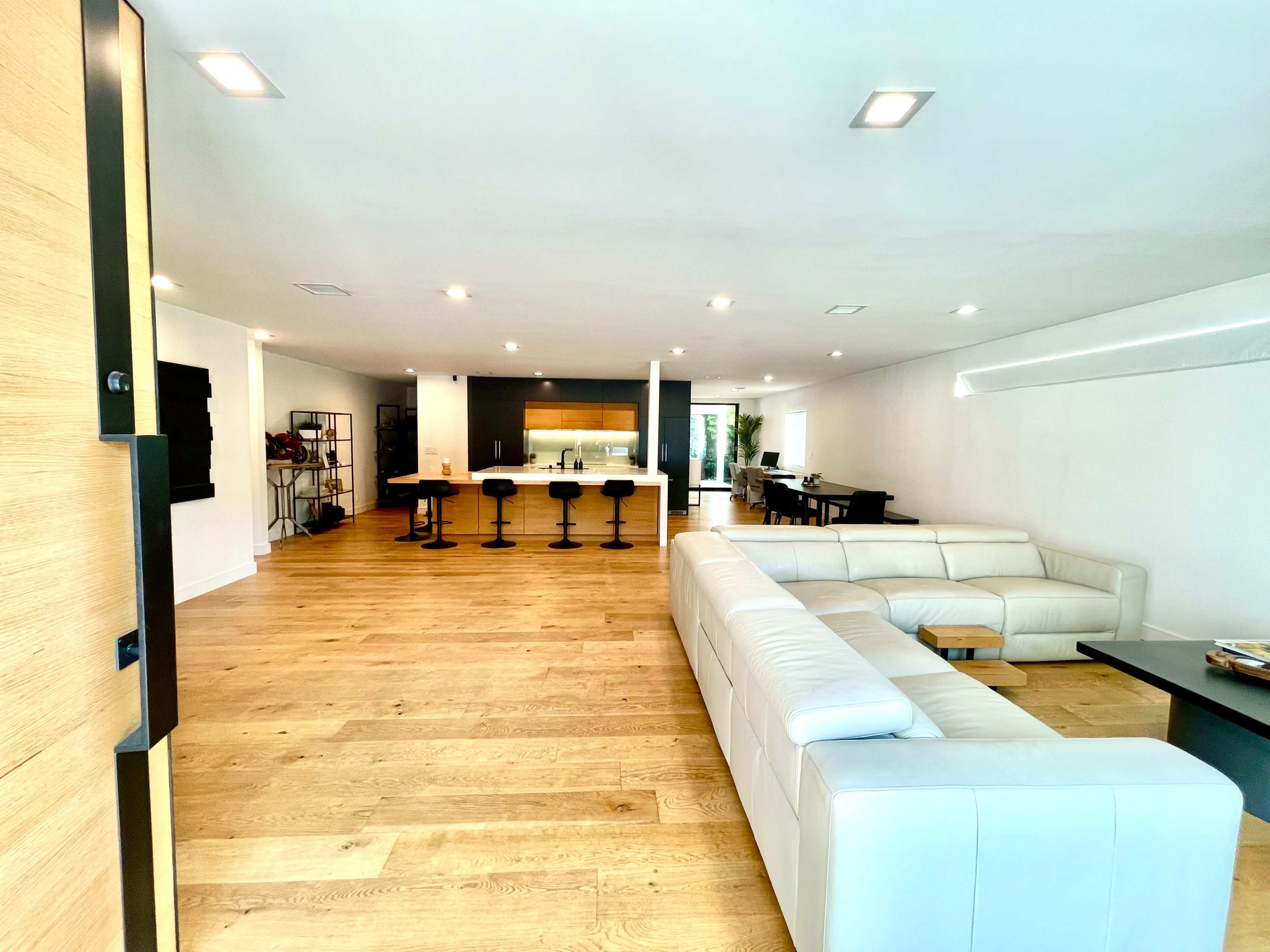 A spacious modern living area with a white sectional sofa facing a sleek kitchen and dining area.