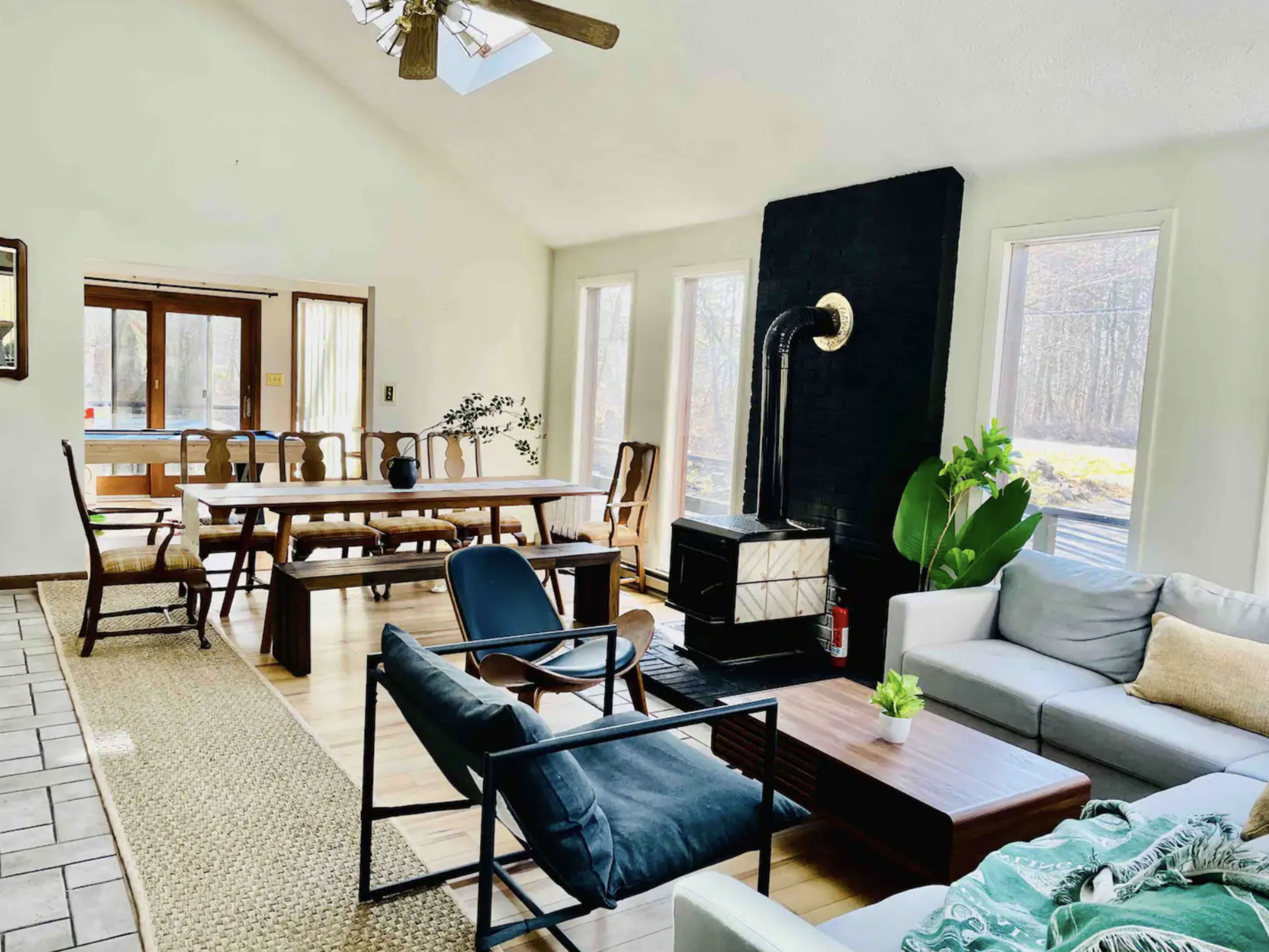A spacious living area with a seating arrangement, a fireplace, and a long dining table surrounded by windows providing natural light.
