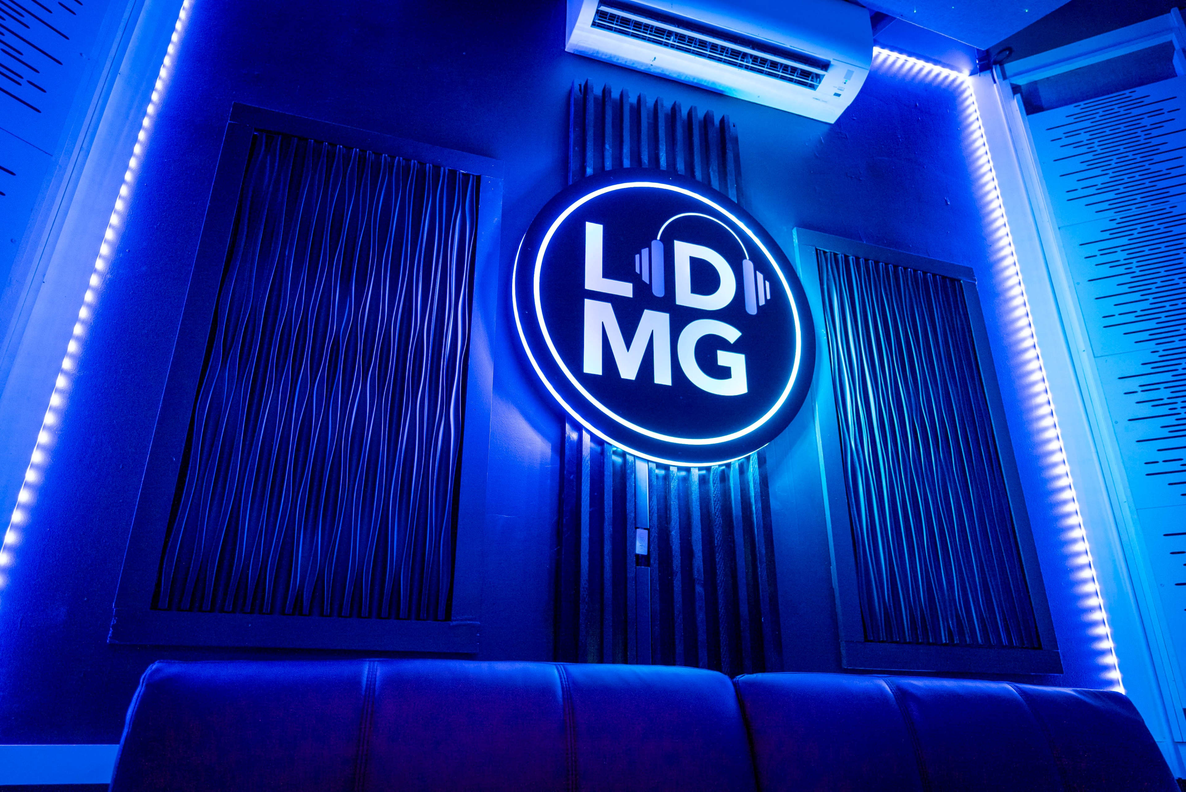 The image displays a blue-lit wall featuring a round, illuminated logo that reads "LDMG," flanked by two vertical panel designs.
