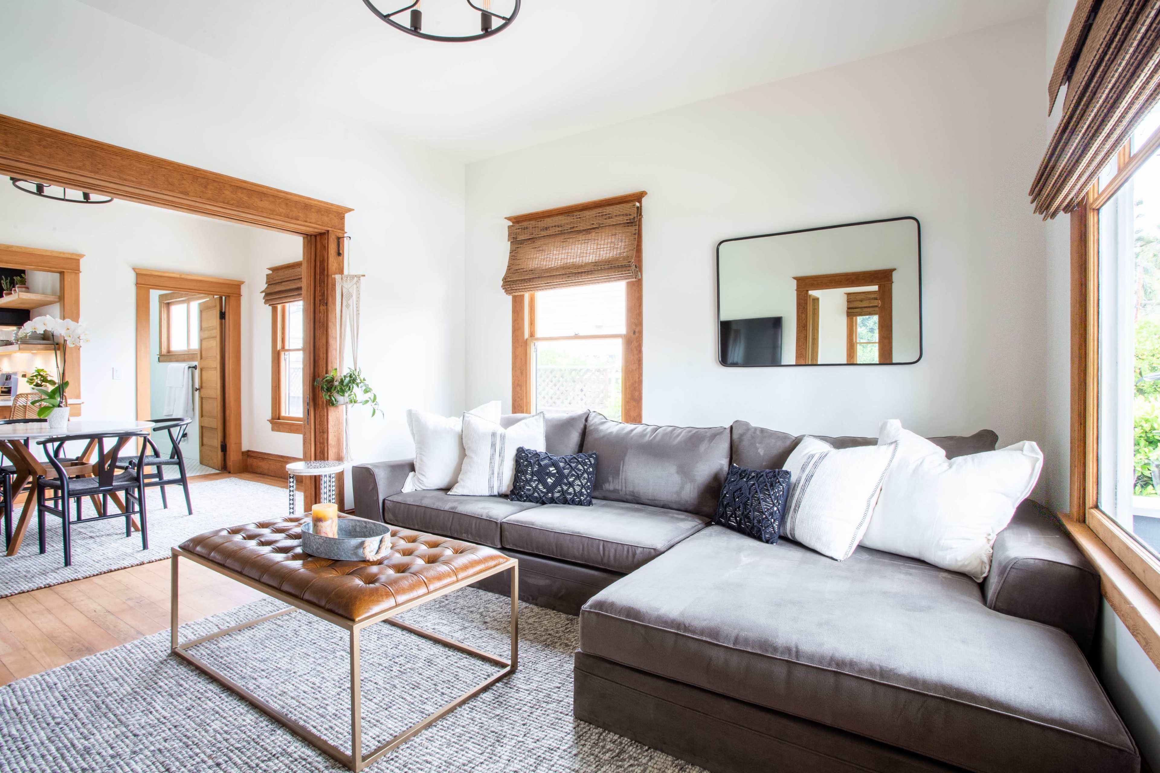 A modern living room features a gray sectional sofa adorned with white pillows, a coffee table, and natural light streaming through the windows.