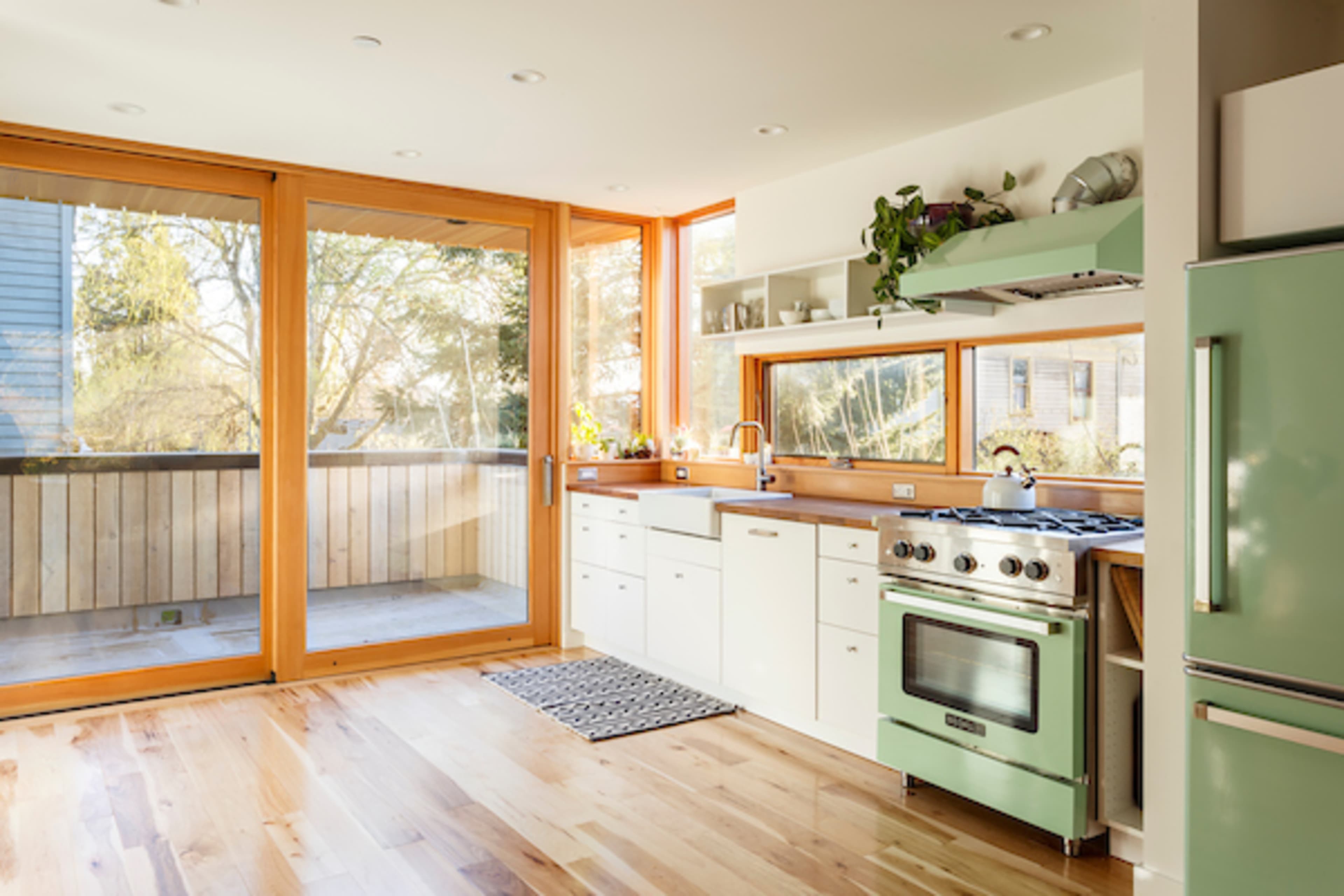 A modern kitchen features a green stove and white cabinetry alongside large windows that open to a deck area.