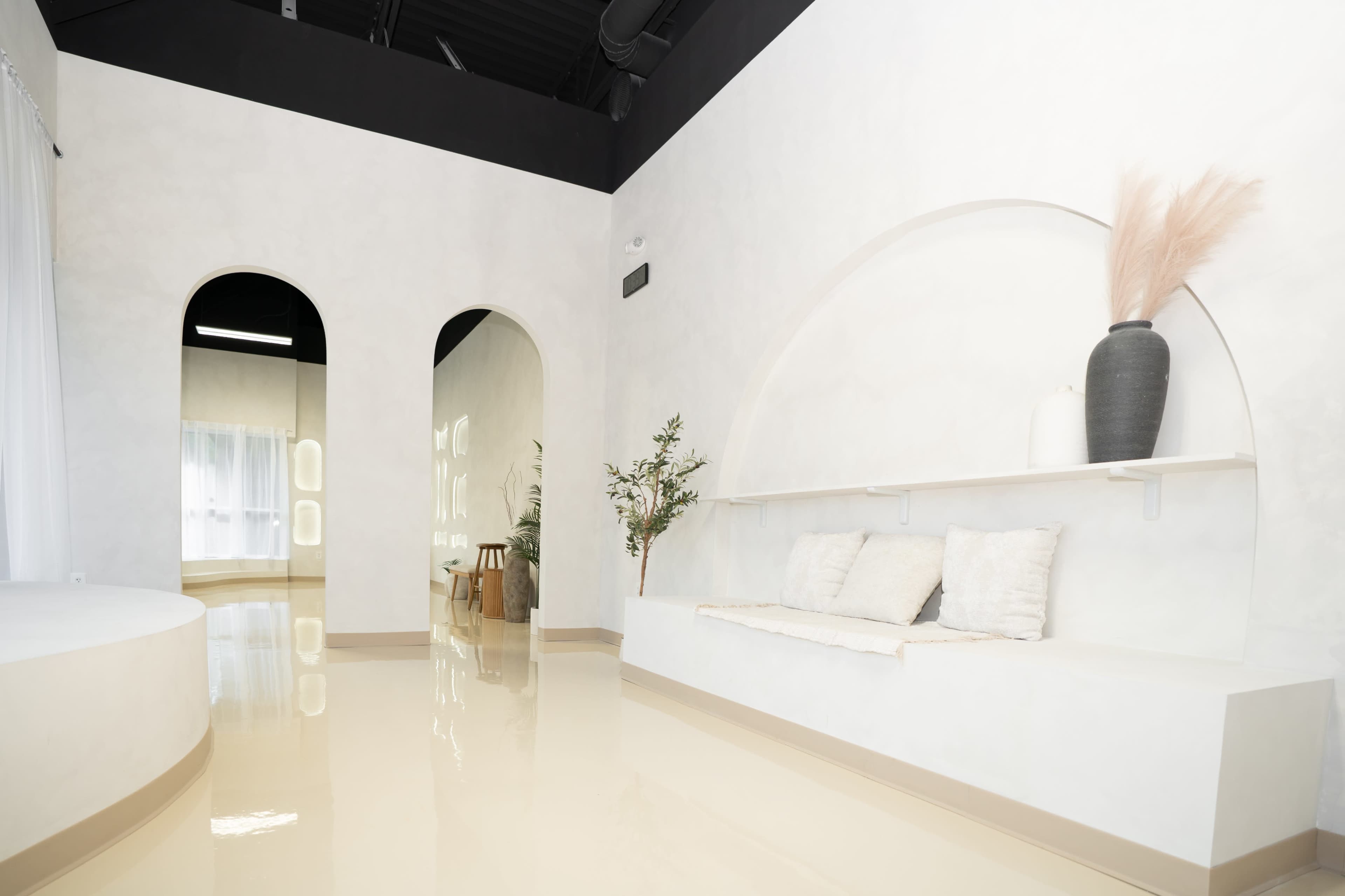 The image shows a modern interior space featuring a smooth, light-colored floor, curved archways, and a minimalist seating area with decorative elements.