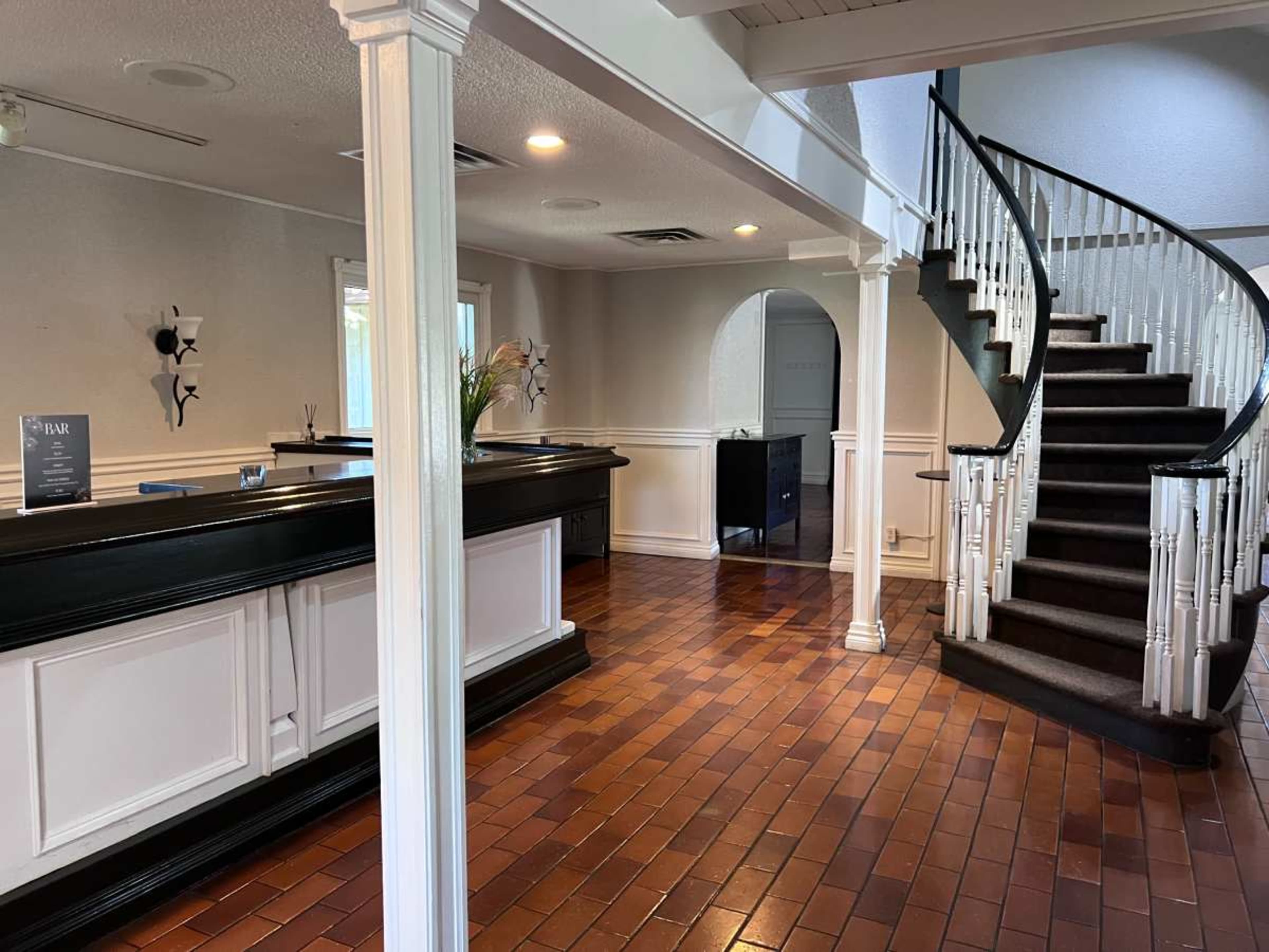 The image shows a reception area with a check-in desk, a winding staircase, and polished wooden flooring.