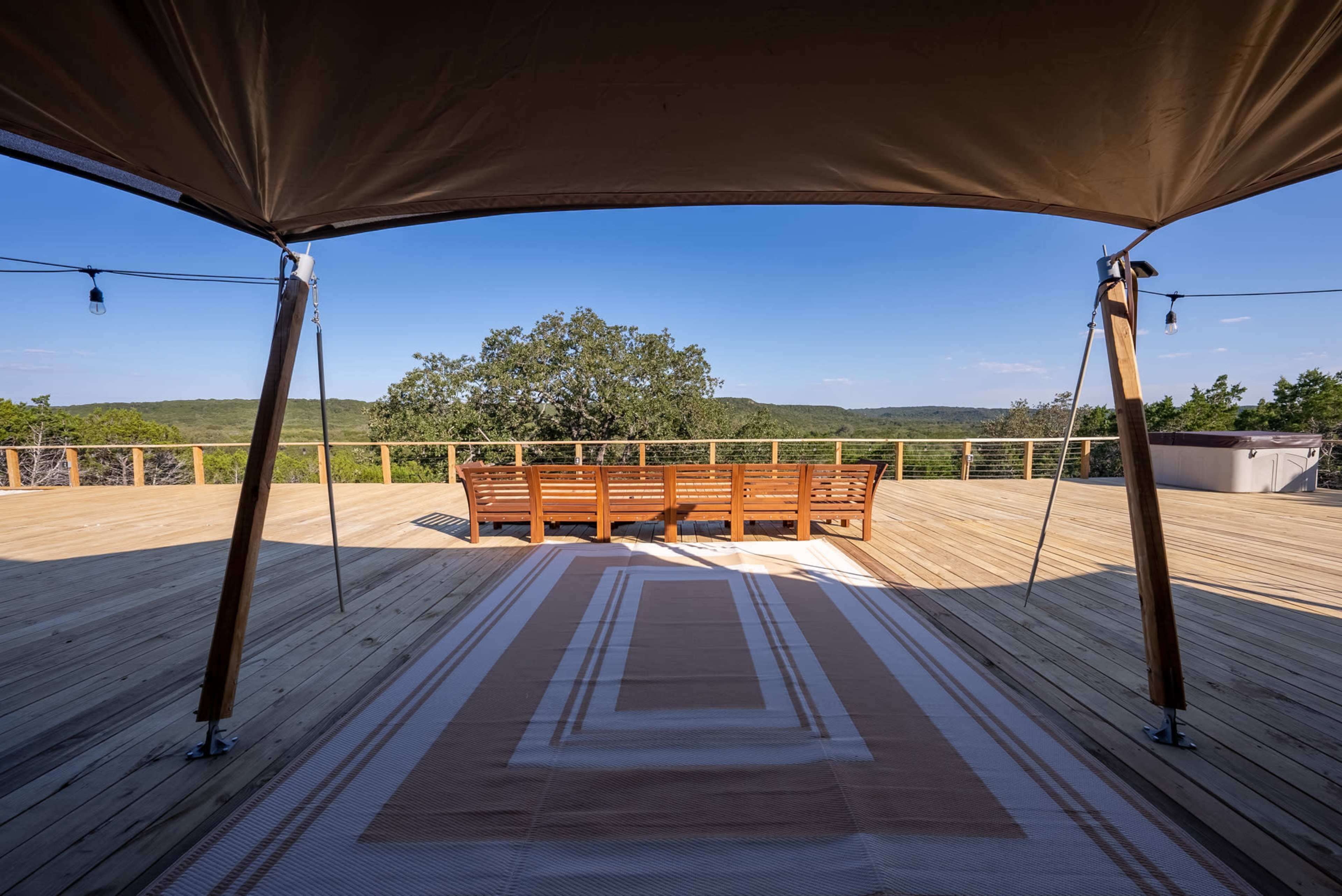 A spacious wooden deck features a set of benches overlooking a green hillside under a clear blue sky.