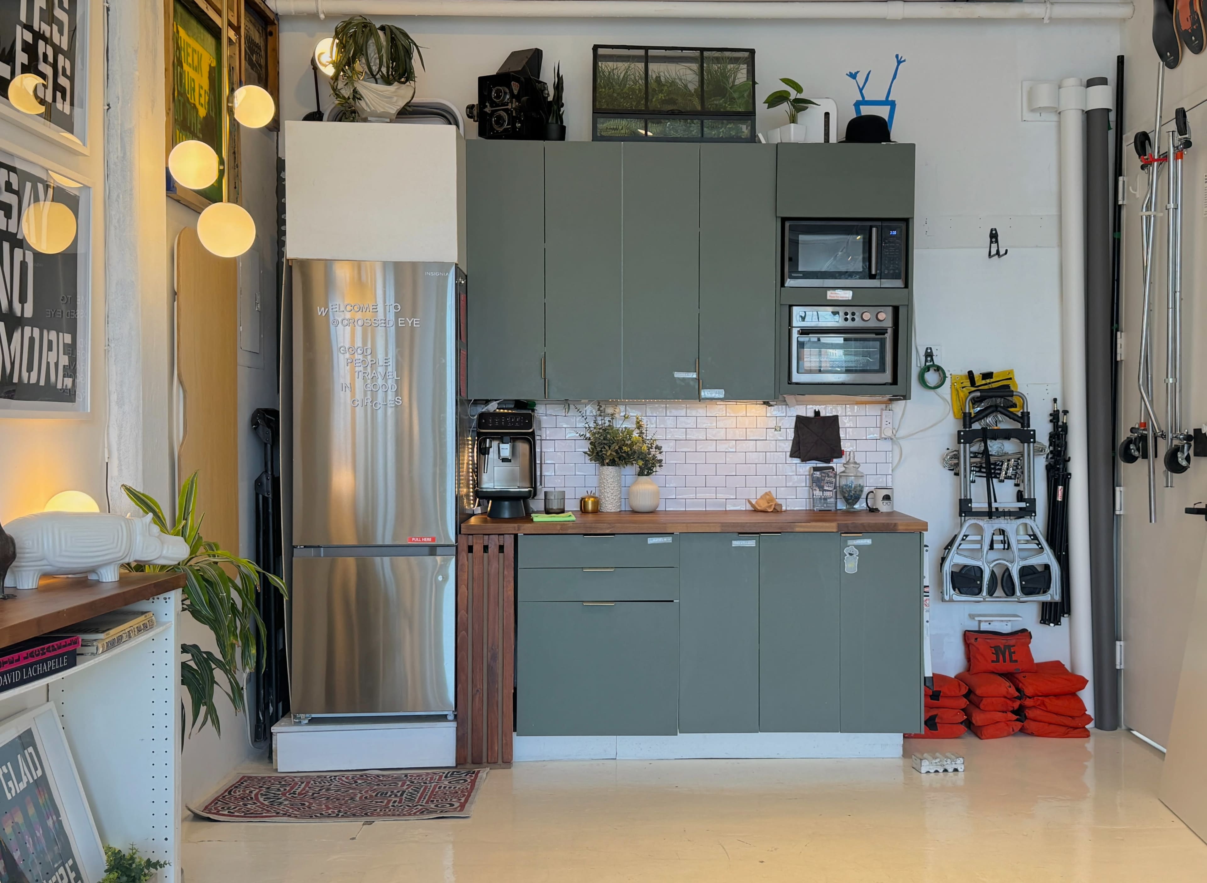 The image shows a modern kitchen with green cabinets, a stainless steel refrigerator, and a variety of kitchen appliances and decor.