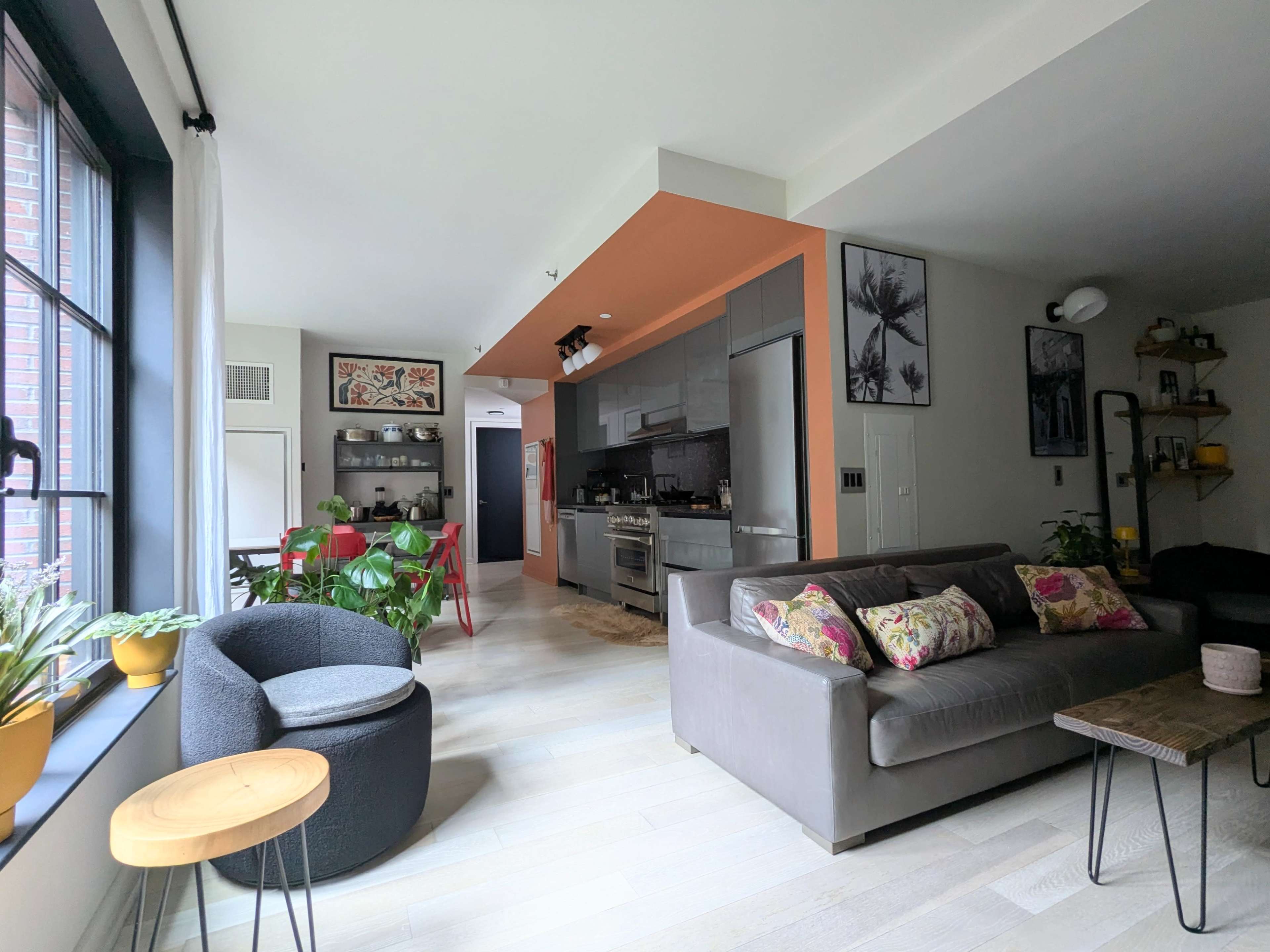 The image shows a modern, open-concept living space featuring a kitchen, dining area, and seating area with various plants and decorative elements.