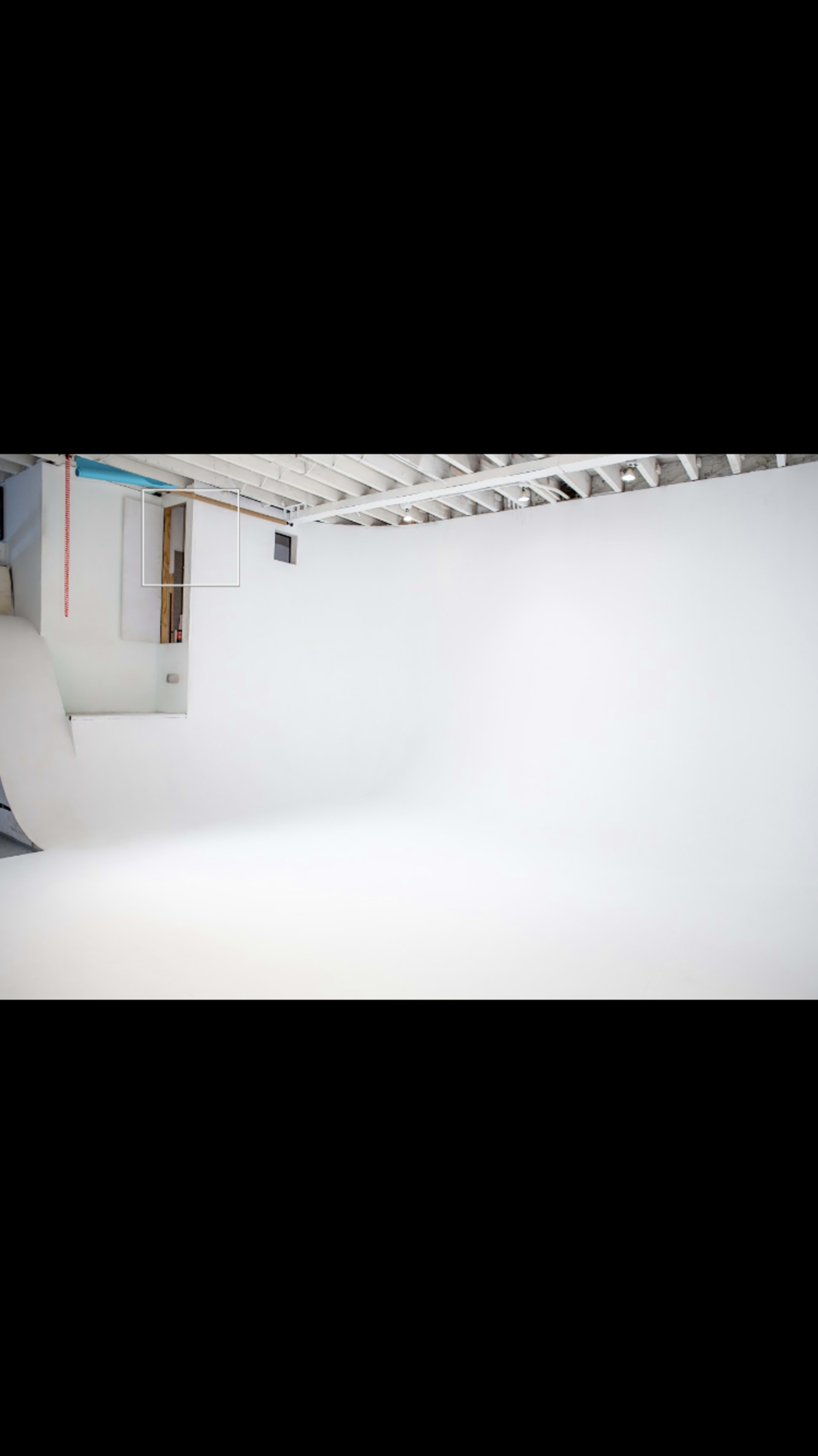 The image shows a spacious photography studio with a plain white background and a partially visible door on the left.