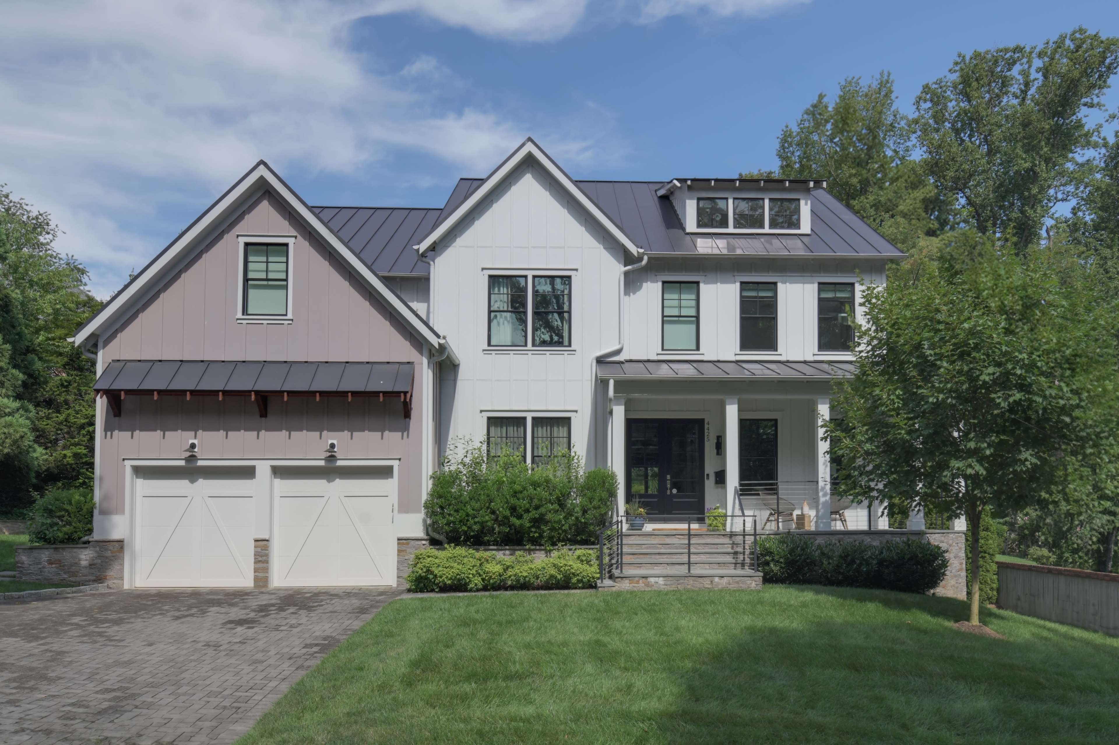 A modern two-story house with a mix of gray and white siding, featuring a front porch, large windows, and a two-car garage.