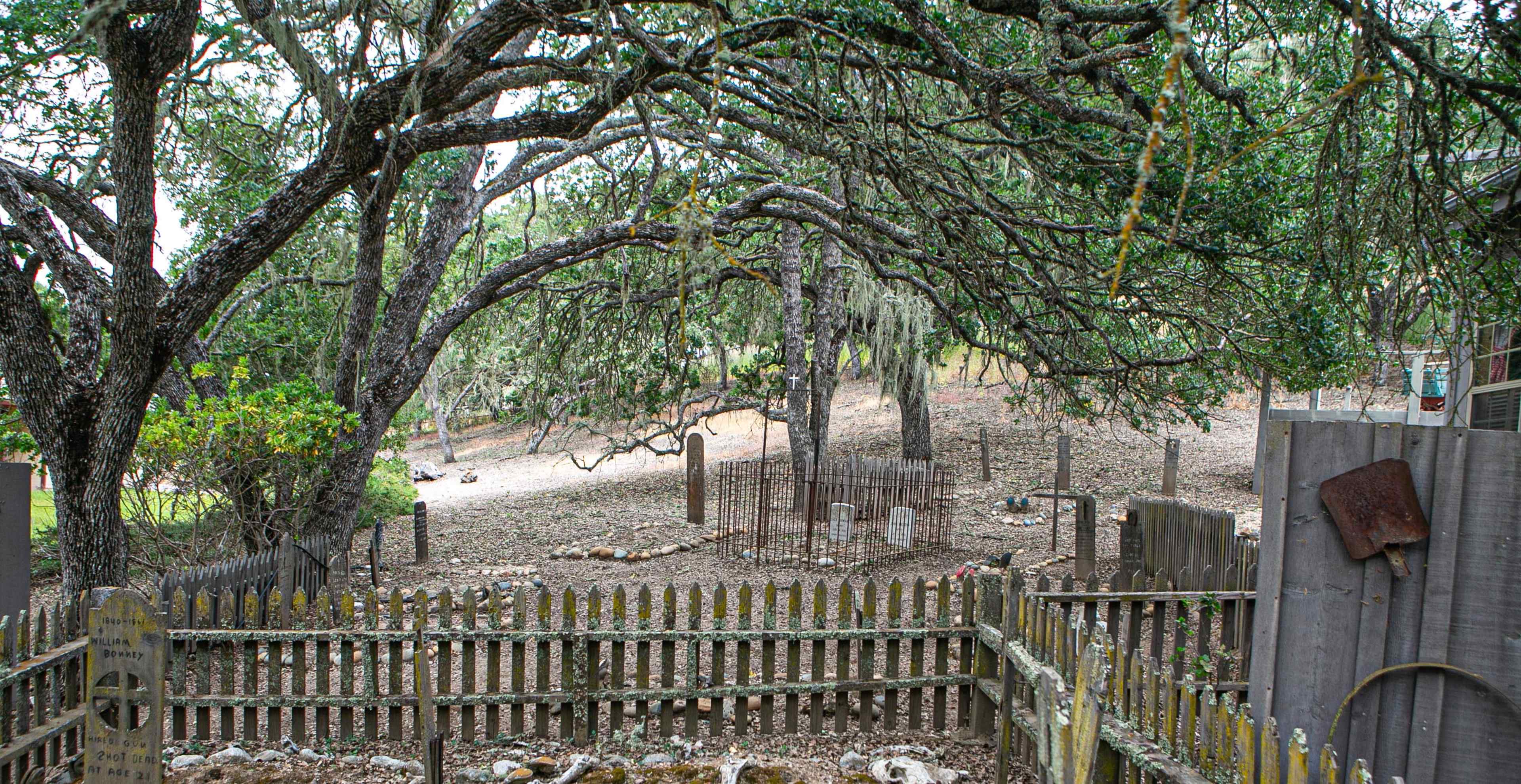 A fenced graveyard surrounded by trees and marked gravestones set in a quiet, wooded area.