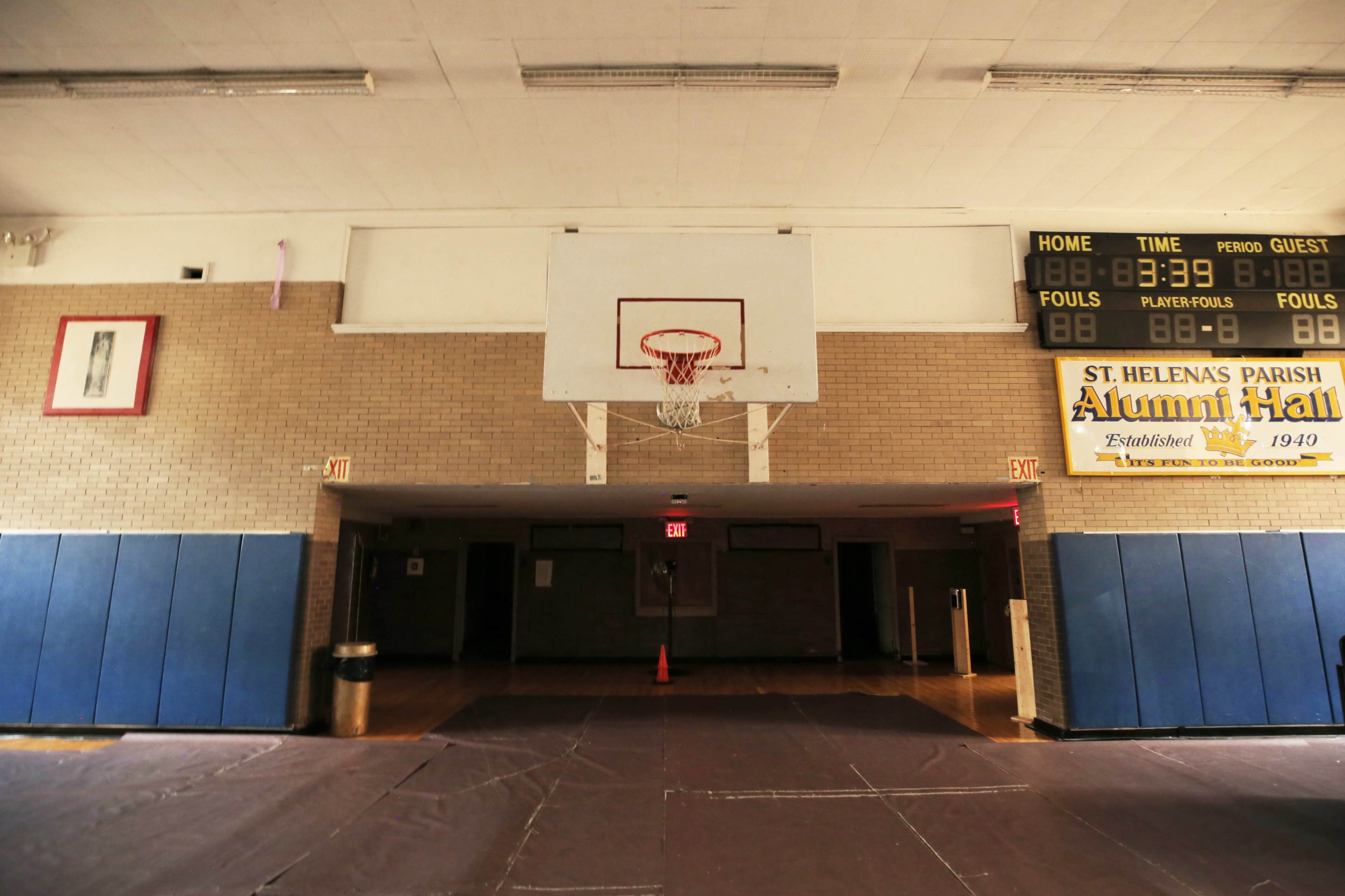 An empty gymnasium with a basketball hoop and a scoreboard displaying a paused game timer.
