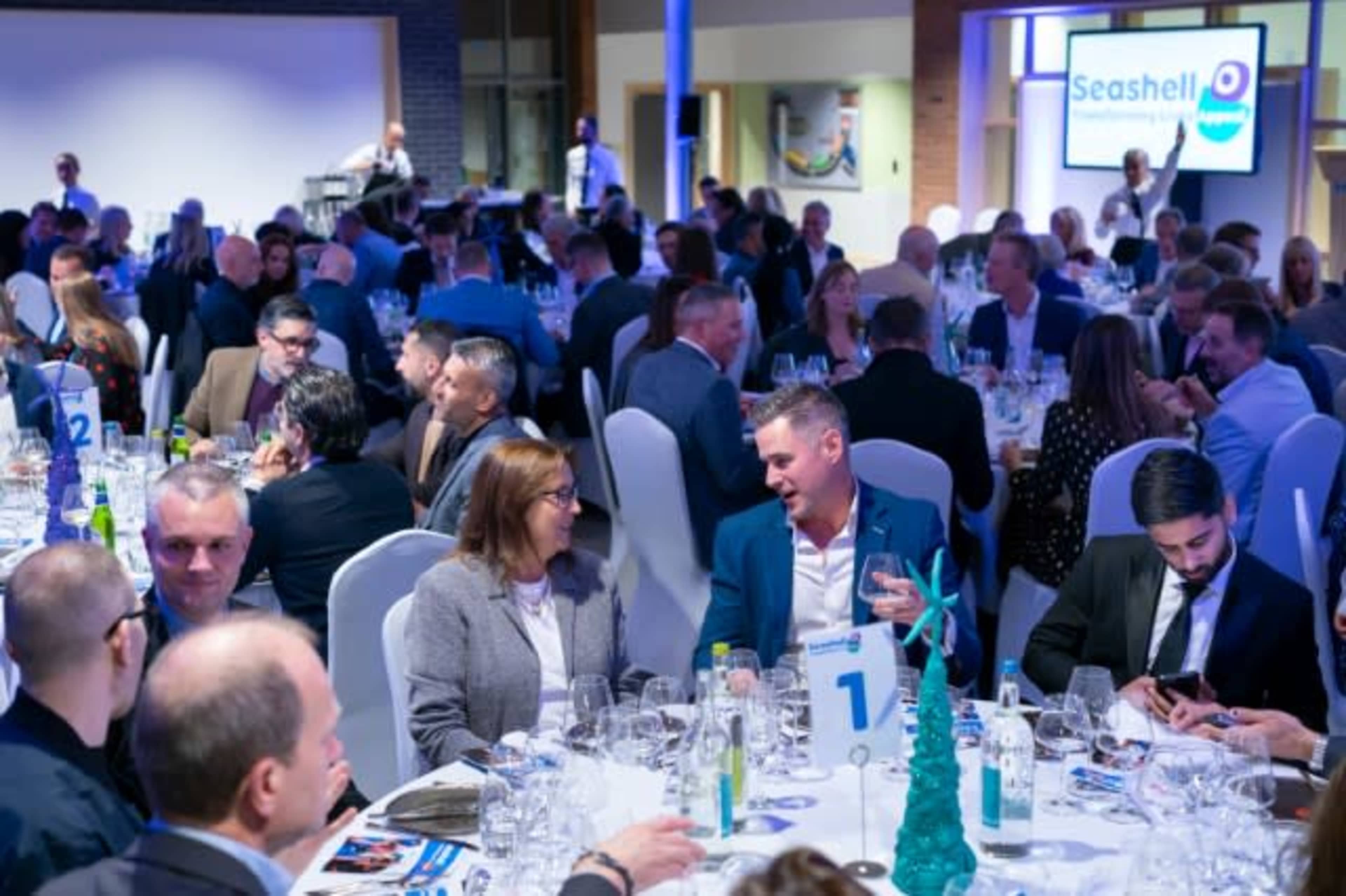 A large group of people is seated around elegantly set tables at a formal dinner event.