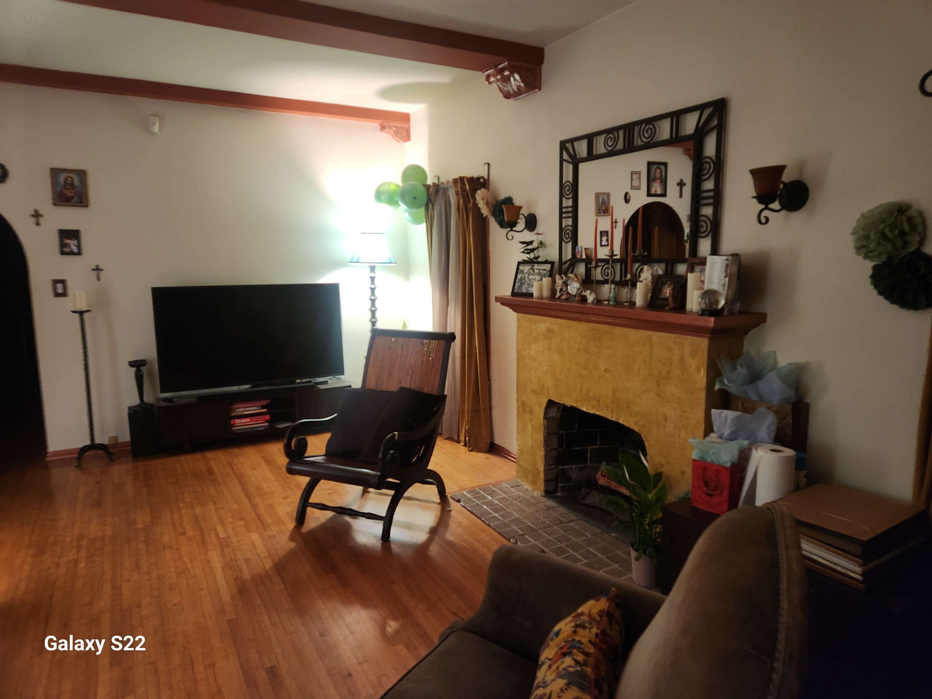 The image shows a living room with a television, a fireplace, a wooden rocking chair, and decorations on the walls.