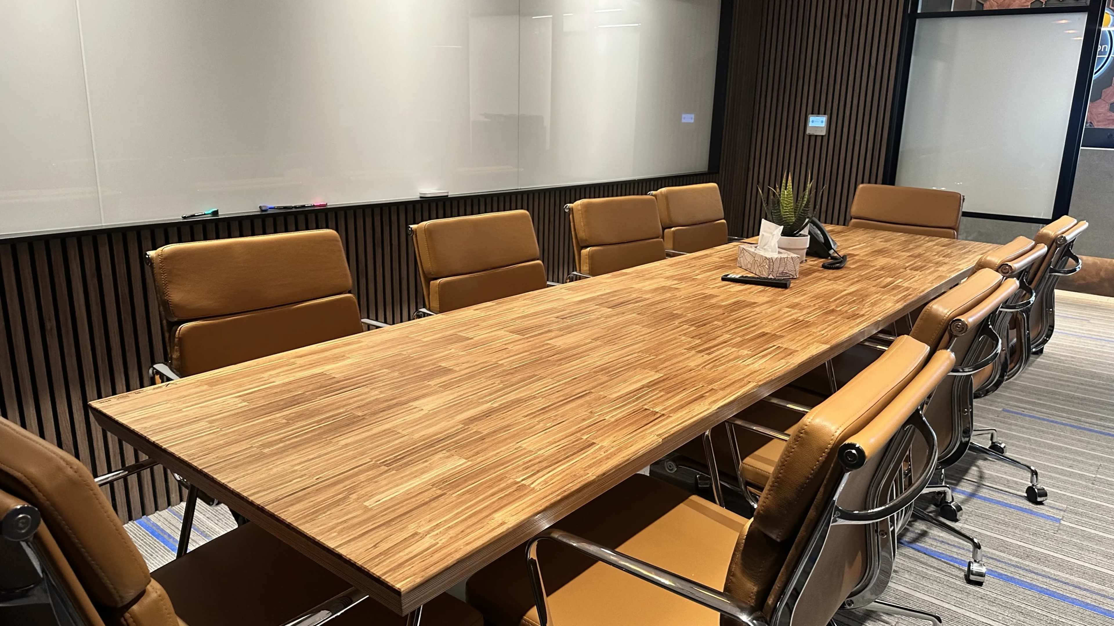 The image shows a modern conference room with a long wooden table, leather chairs, and a whiteboard in the background.