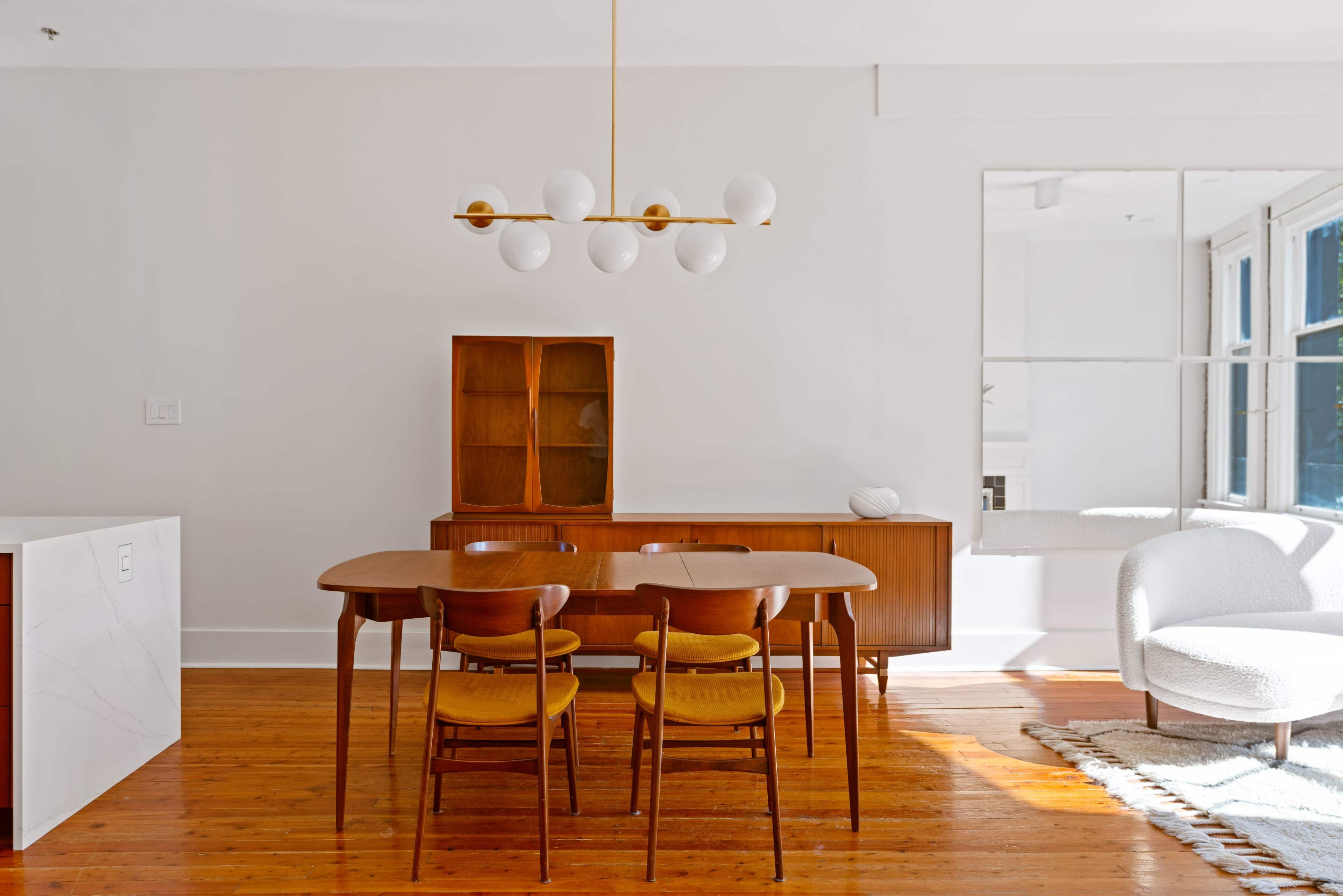A modern dining area featuring a wooden table with four chairs, a sideboard, and a ceiling light fixture with round white bulbs.