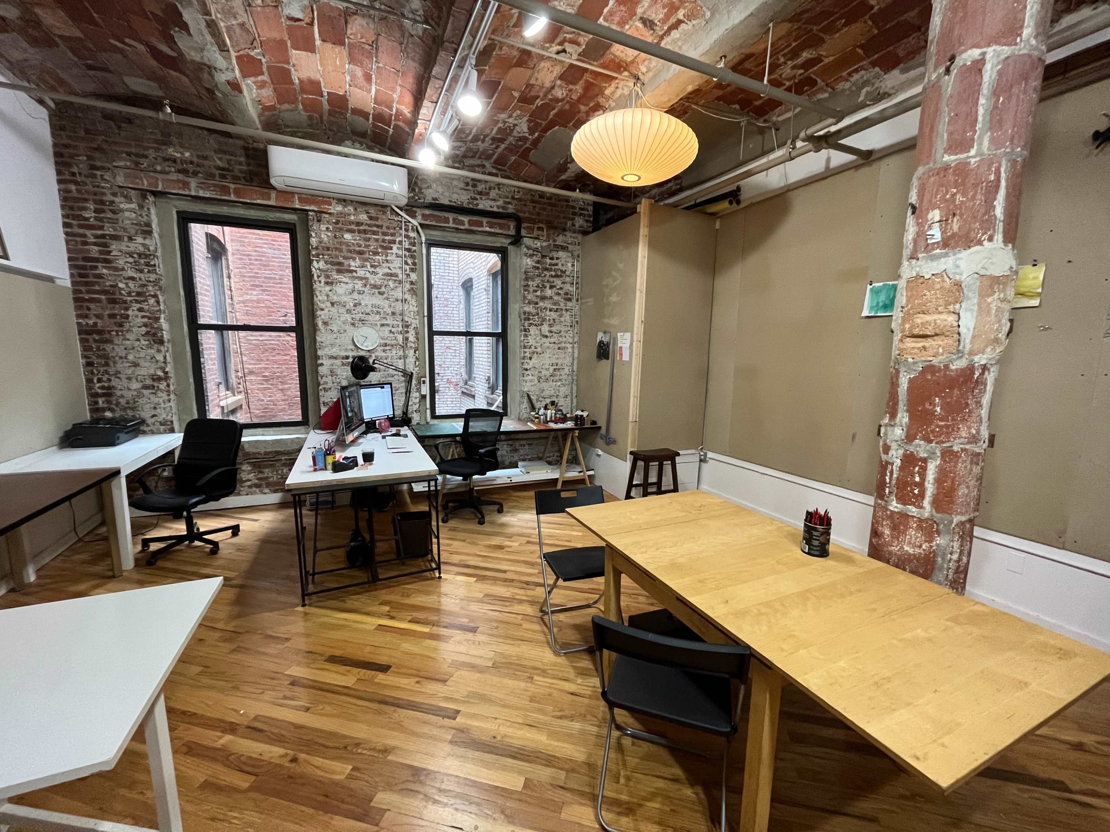 A spacious office with exposed brick walls, wooden flooring, and two distinct work areas containing desks and chairs.