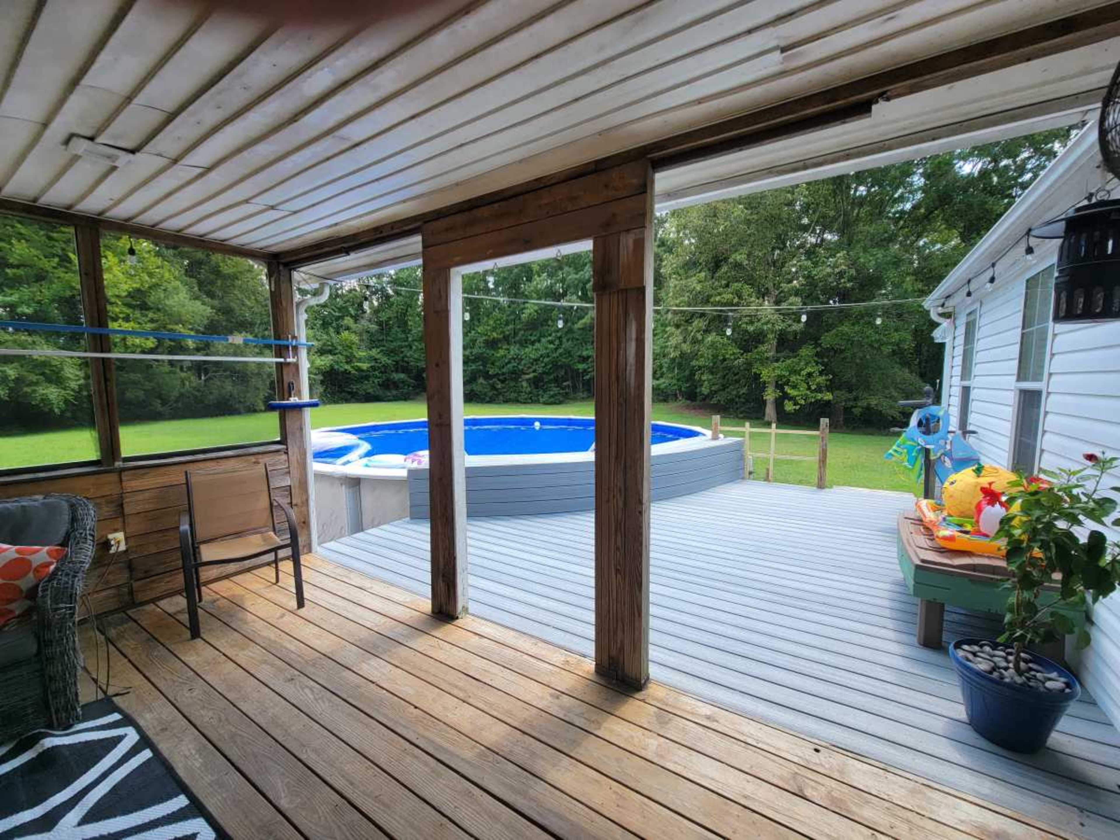 A wooden porch with a chair overlooks a backyard pool surrounded by greenery.