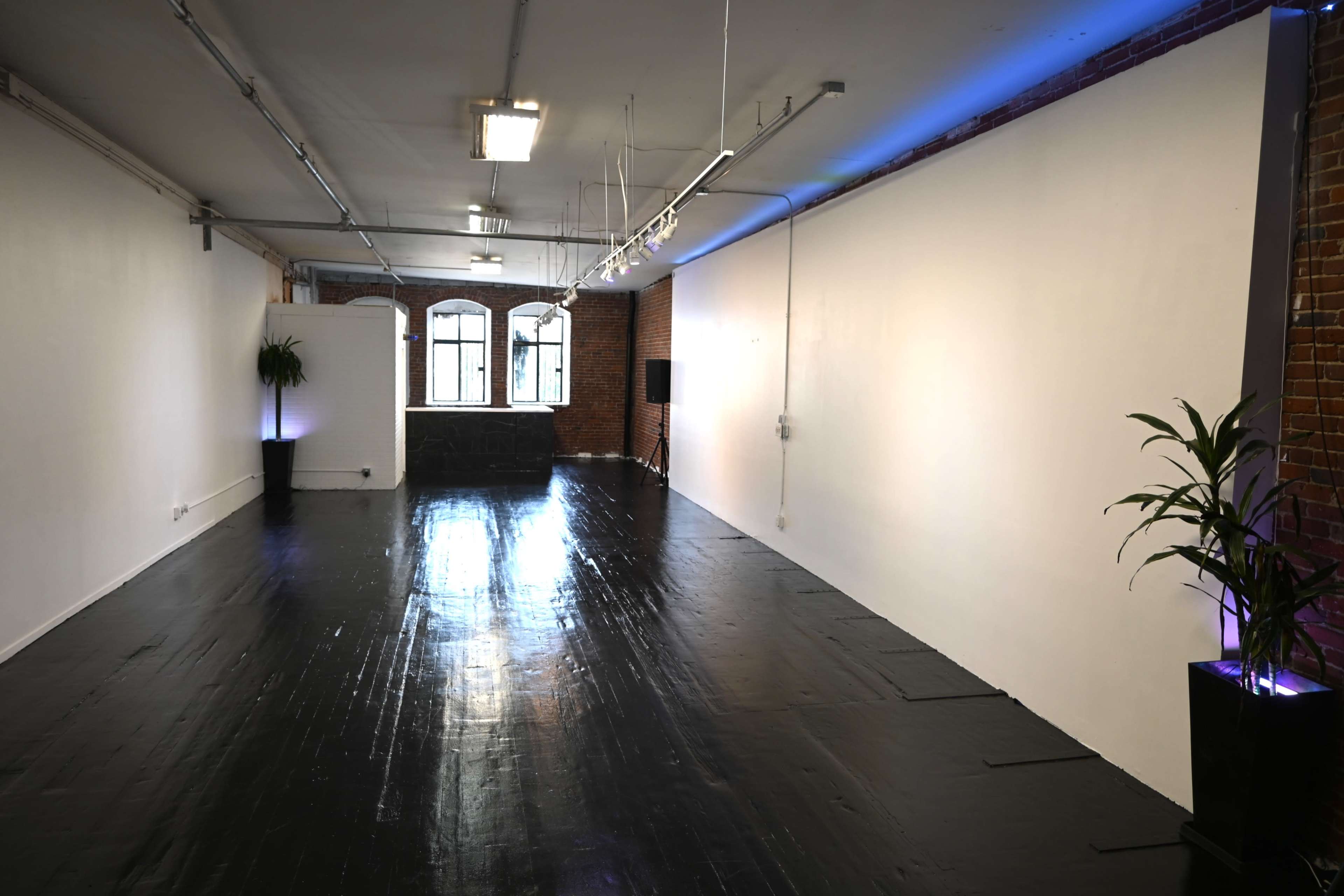 A spacious, minimalist interior with a black floor, exposed brick walls, and a large window at one end.