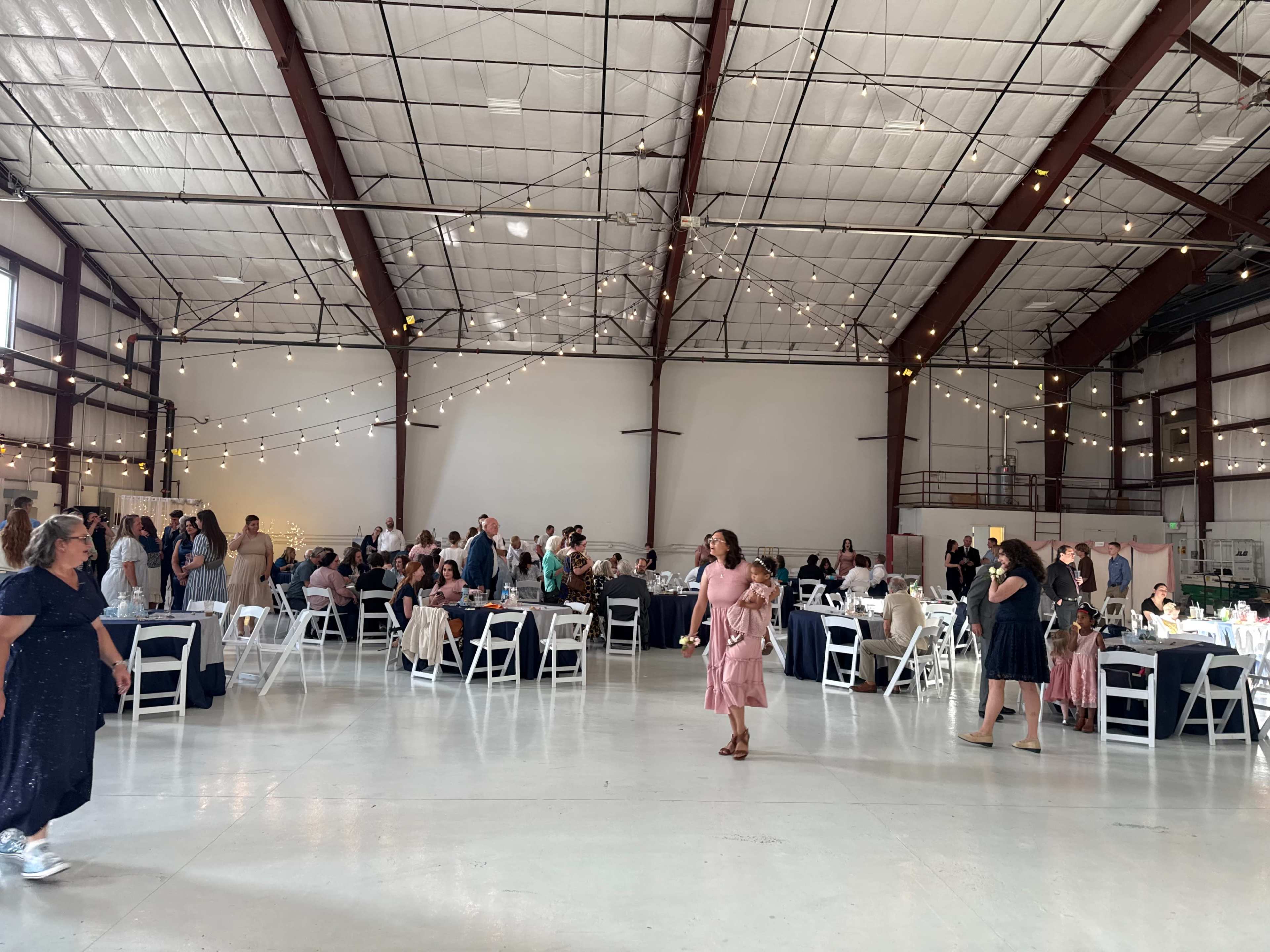 A spacious indoor venue is filled with guests seated at round tables, with some people socializing and mingling in the background.