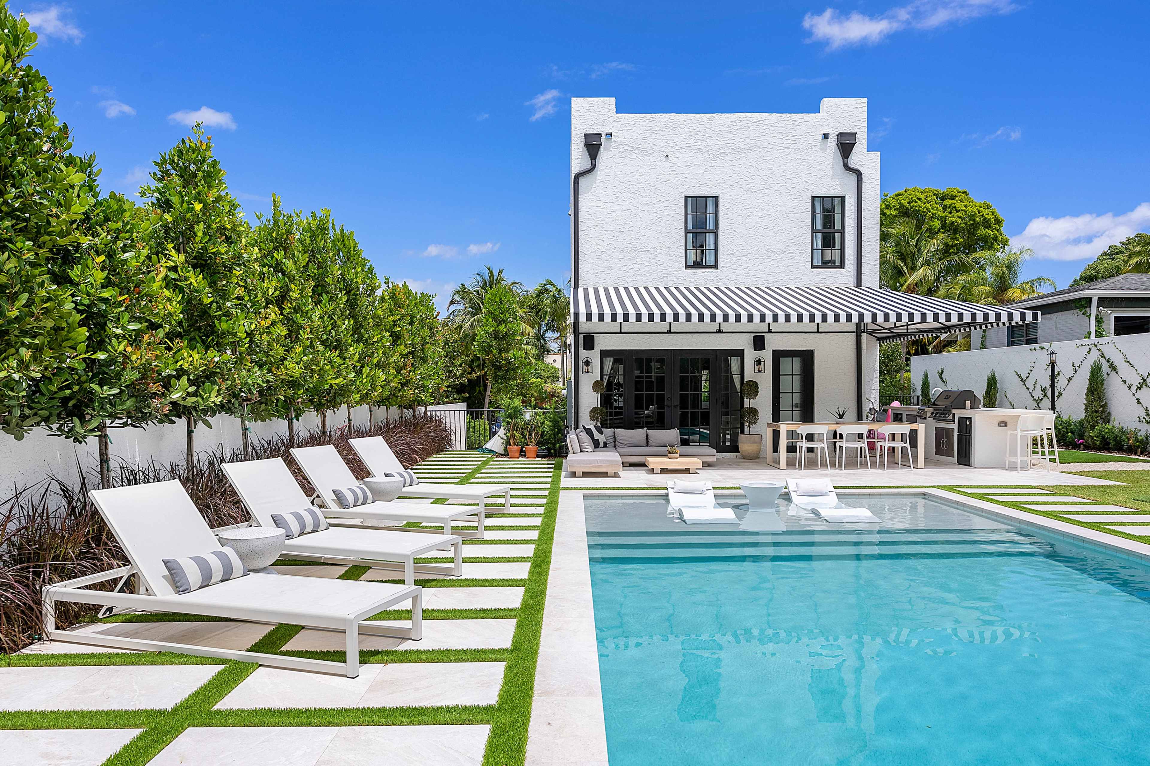 The image shows a modern backyard with a swimming pool, lounge chairs, and a two-story white house surrounded by greenery.