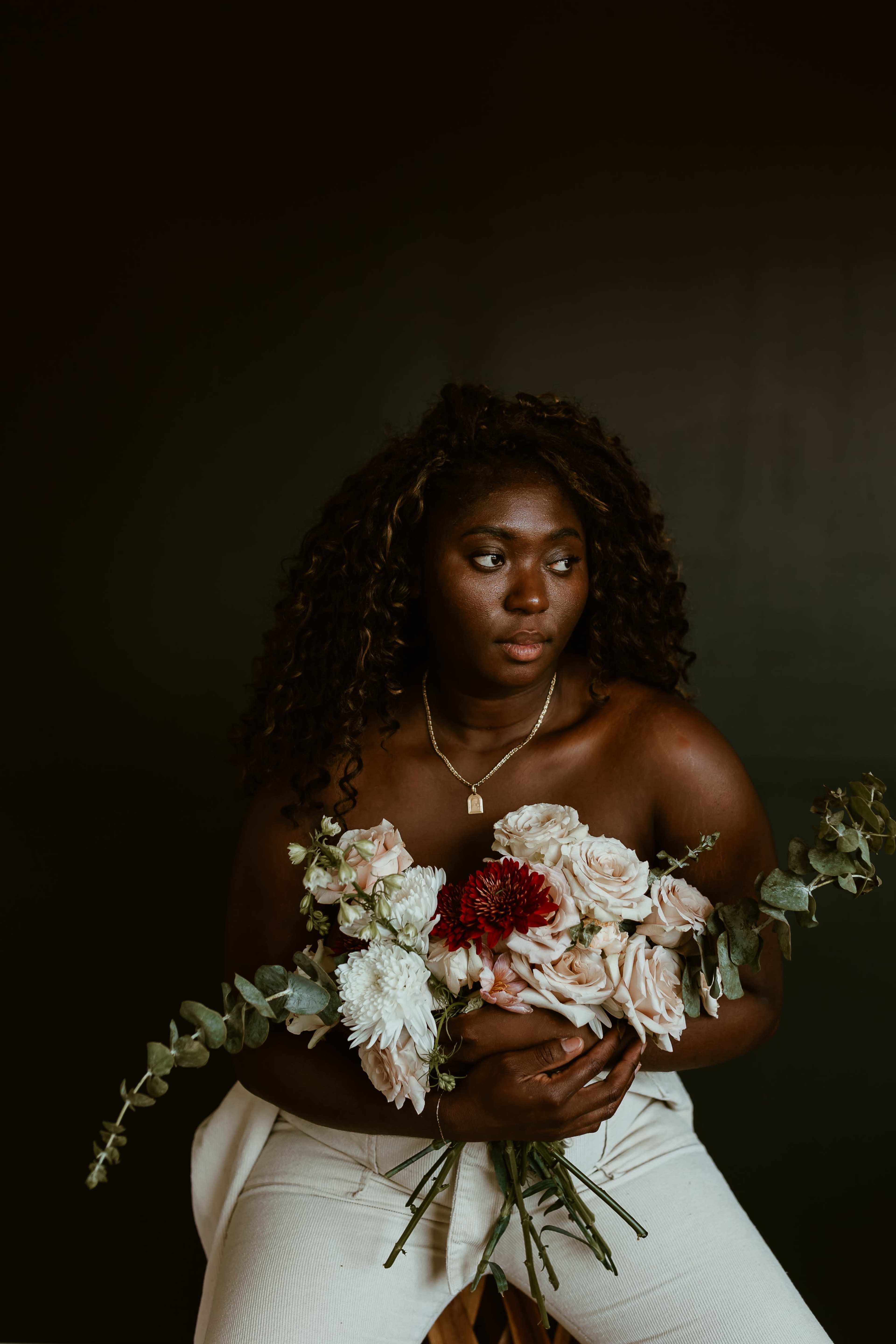 A person holds a bouquet of flowers while seated against a dark backdrop.