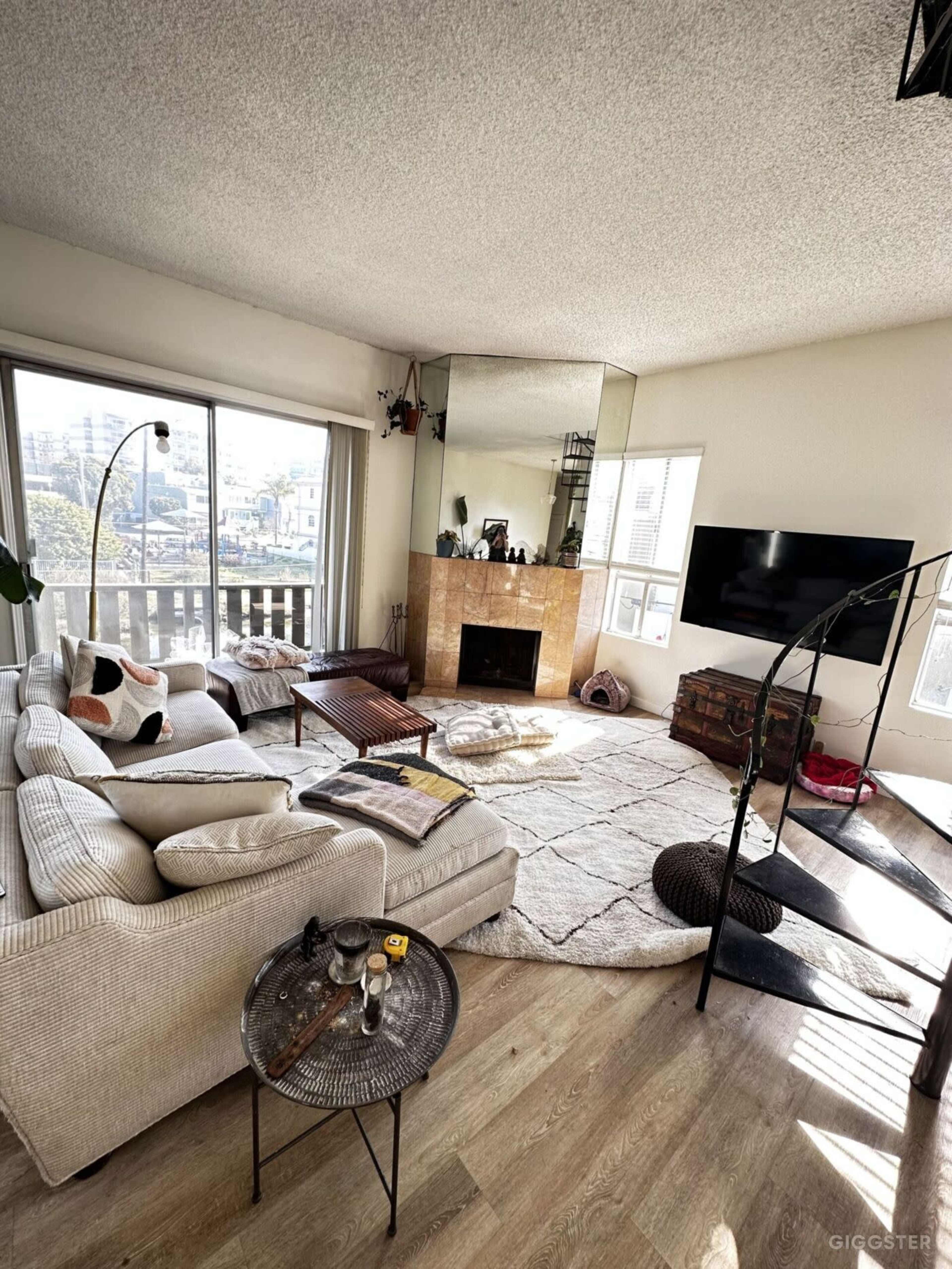 The living room features a sectional sofa, a coffee table, a fireplace, and a large mirror, with large windows allowing natural light to fill the space.