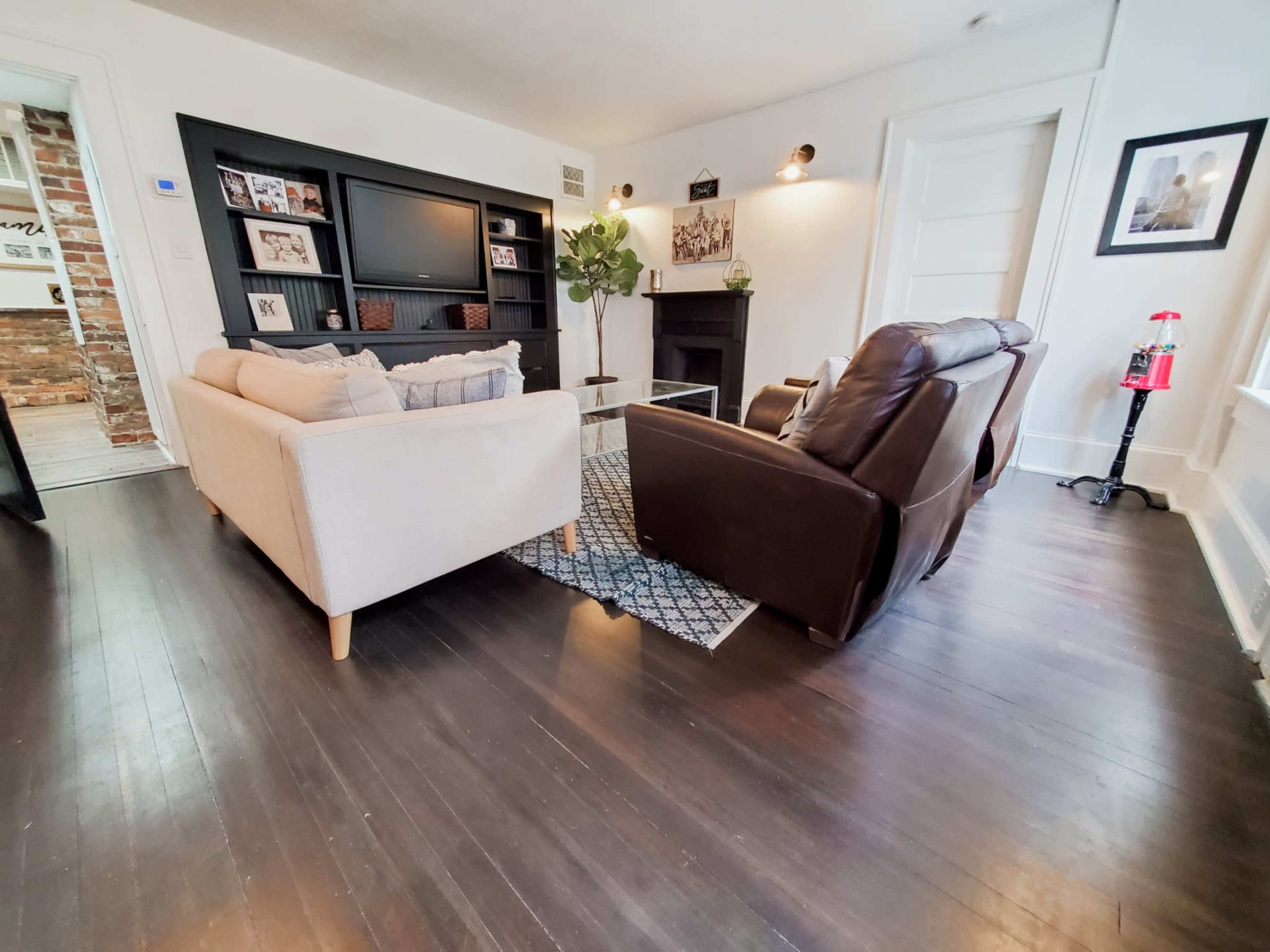 A living room features a beige couch, a brown recliner, a television unit with shelves, and a small coffee table on a patterned rug.