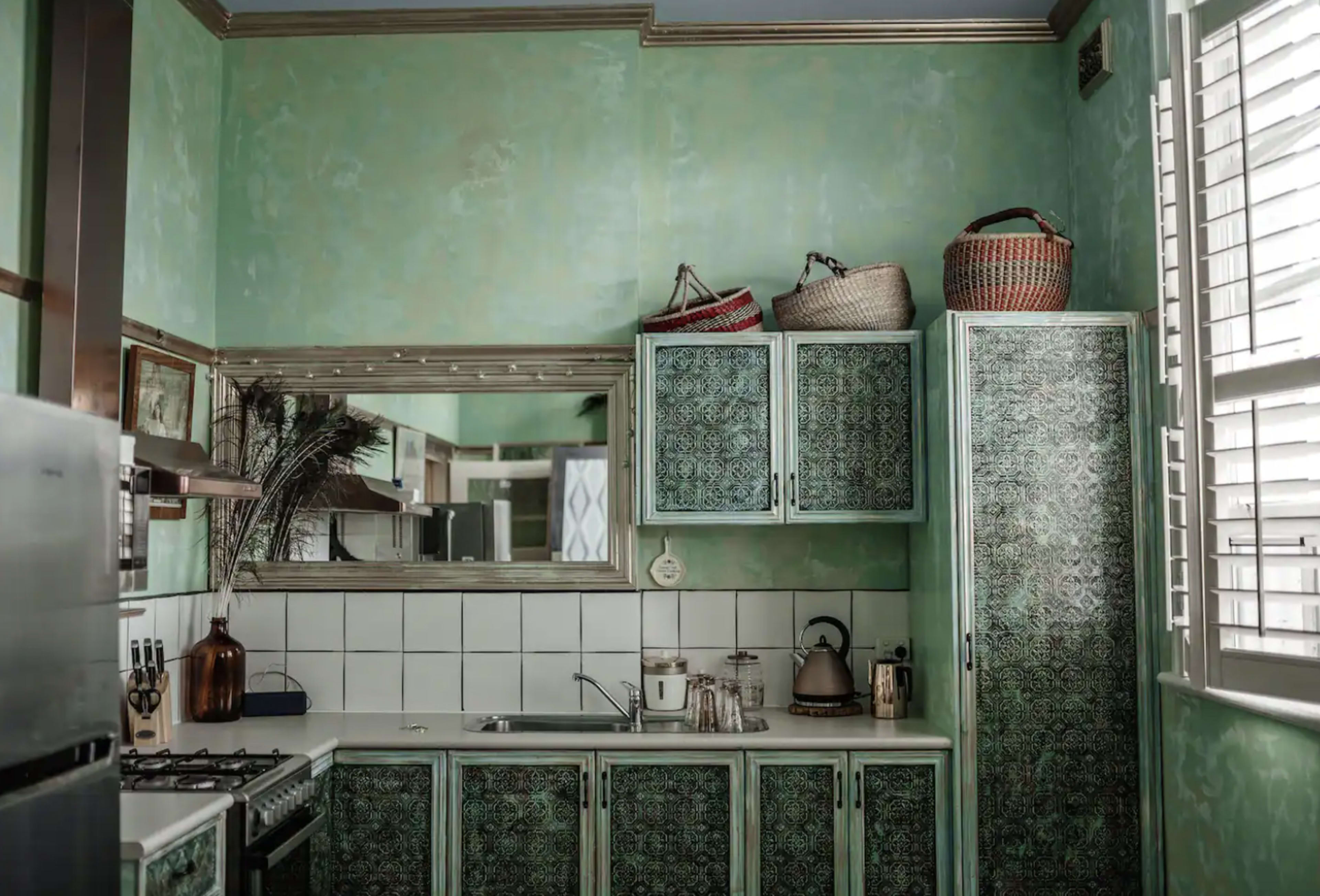 The image shows a kitchen with green walls, tiled countertops, and vintage-style cabinets adorned with a patterned finish.