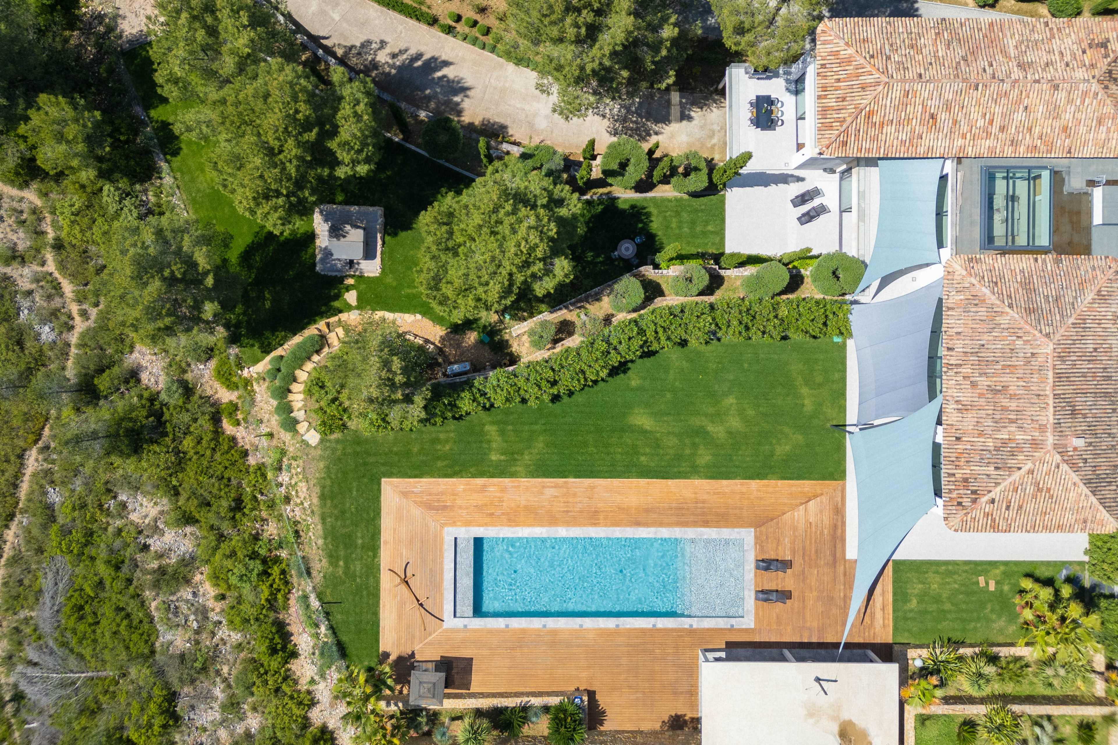 The image shows an aerial view of a backyard featuring a swimming pool surrounded by wooden decking, landscaped gardens, and a house with a tiled roof.