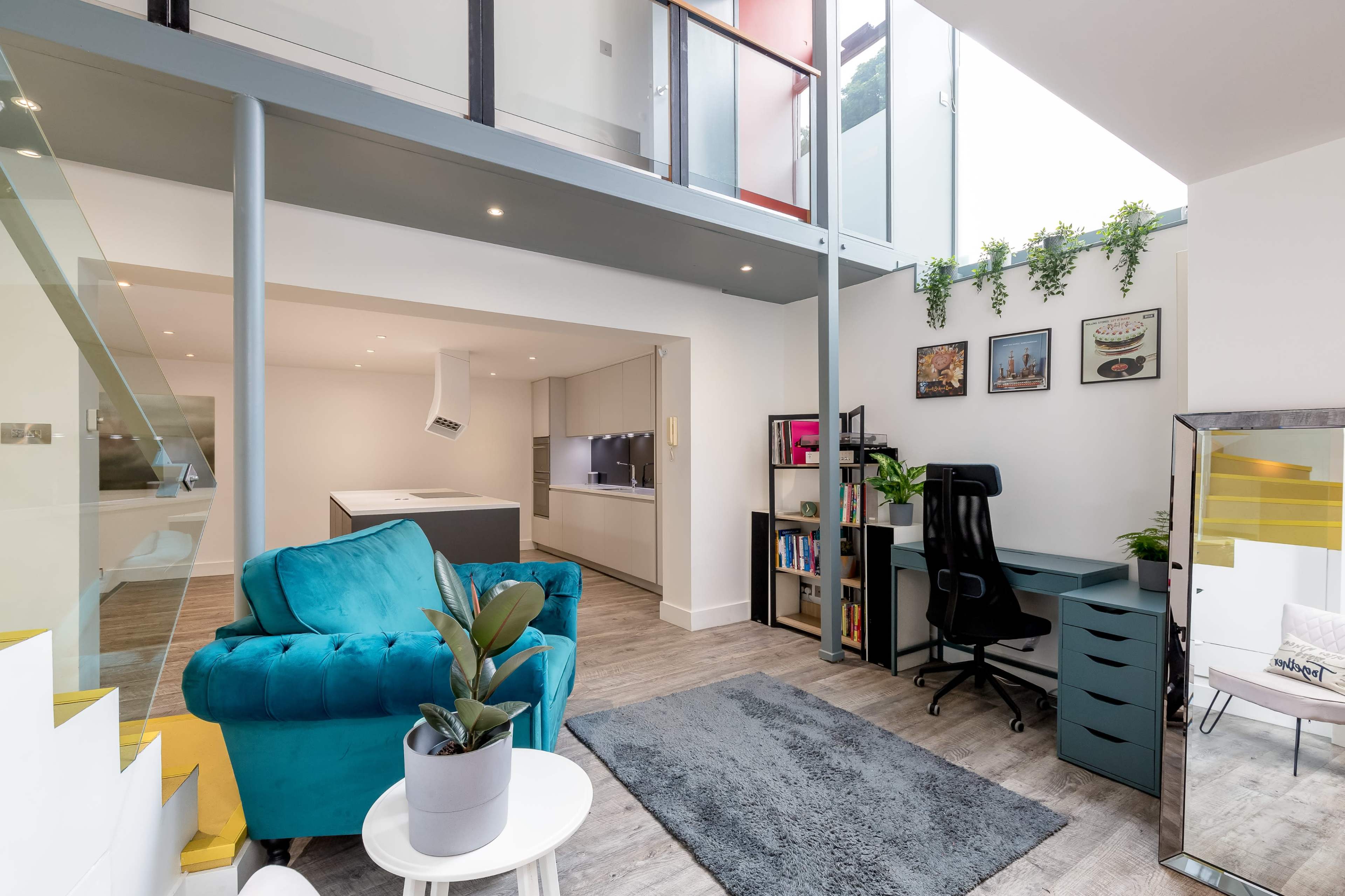 A modern, open-concept living space with a turquoise couch, a desk setup, and a kitchen area visible in the background.