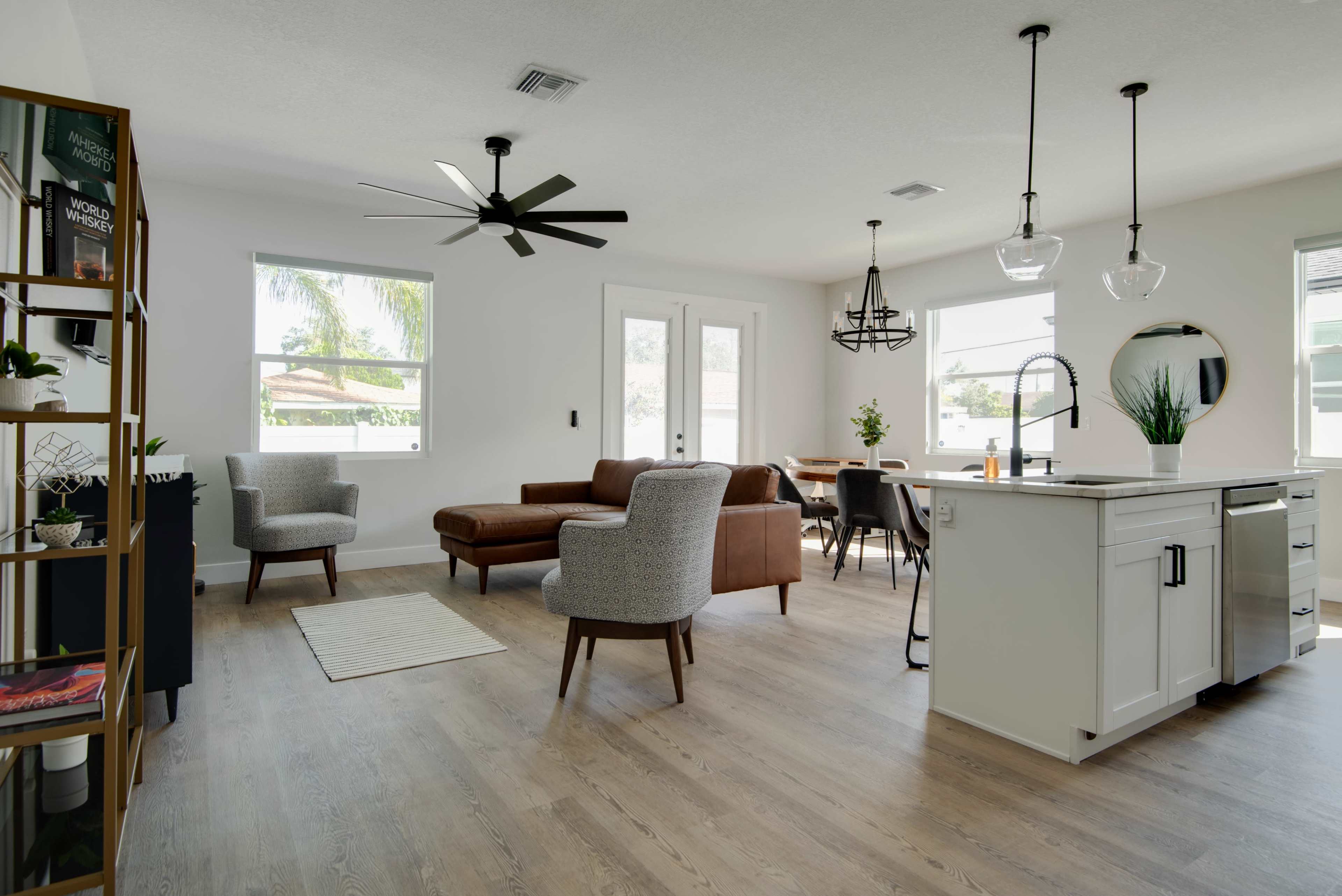 A modern living and dining area with a sectional sofa, dining table, ceiling fans, and large windows.