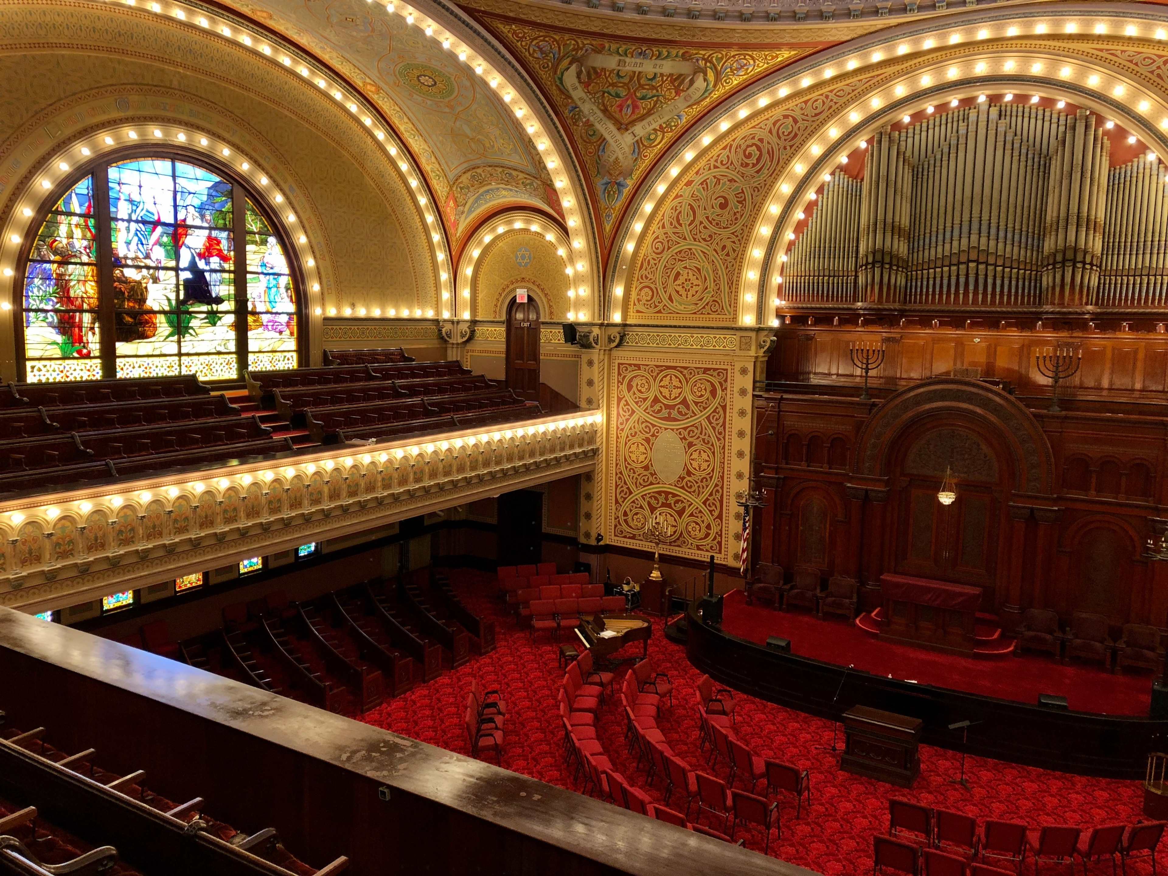A grand legislative chamber with ornate architecture, red seating, and a large stained glass window.