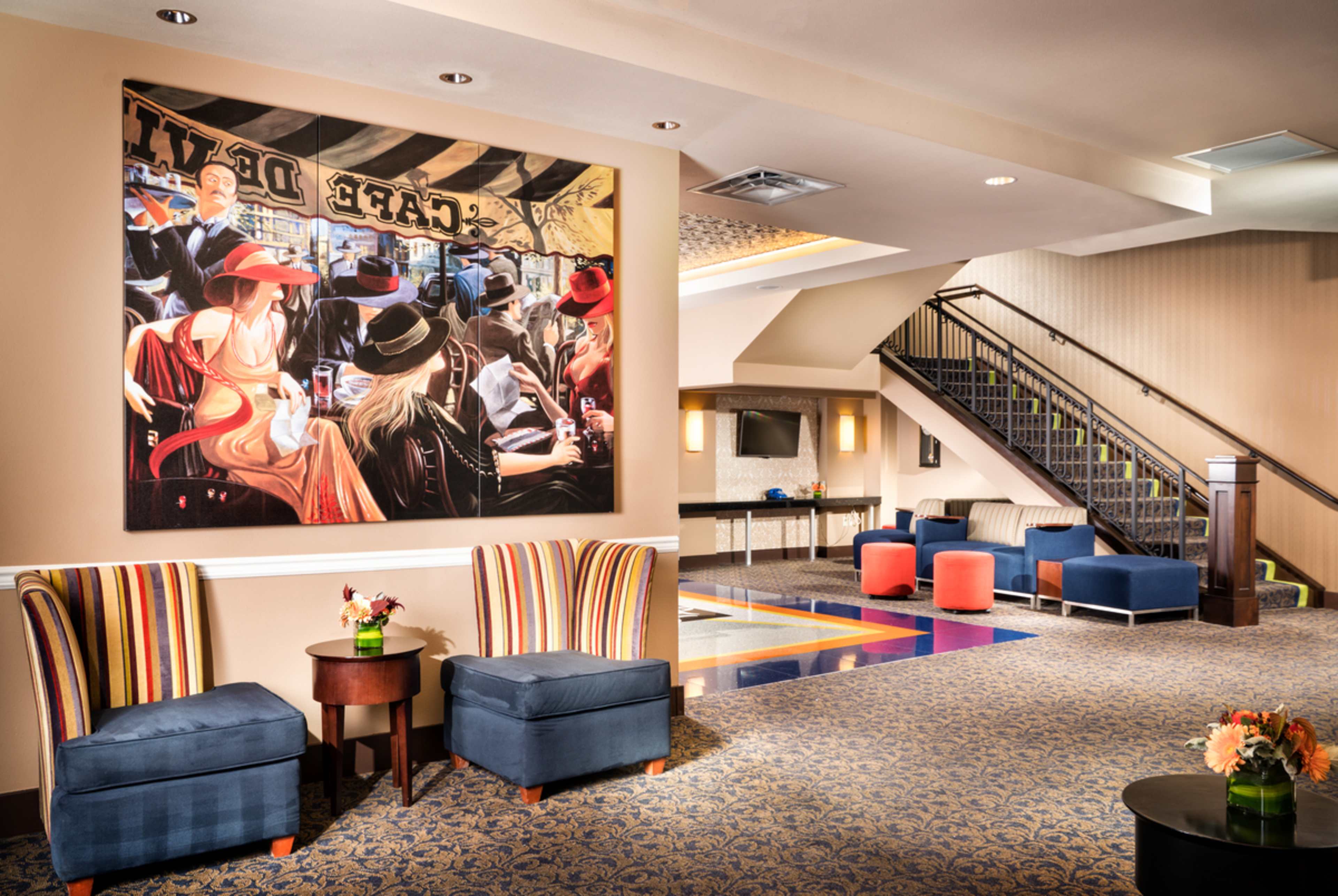 A hotel lobby featuring two striped chairs, a large painting on the wall, and a staircase leading to an upper level.