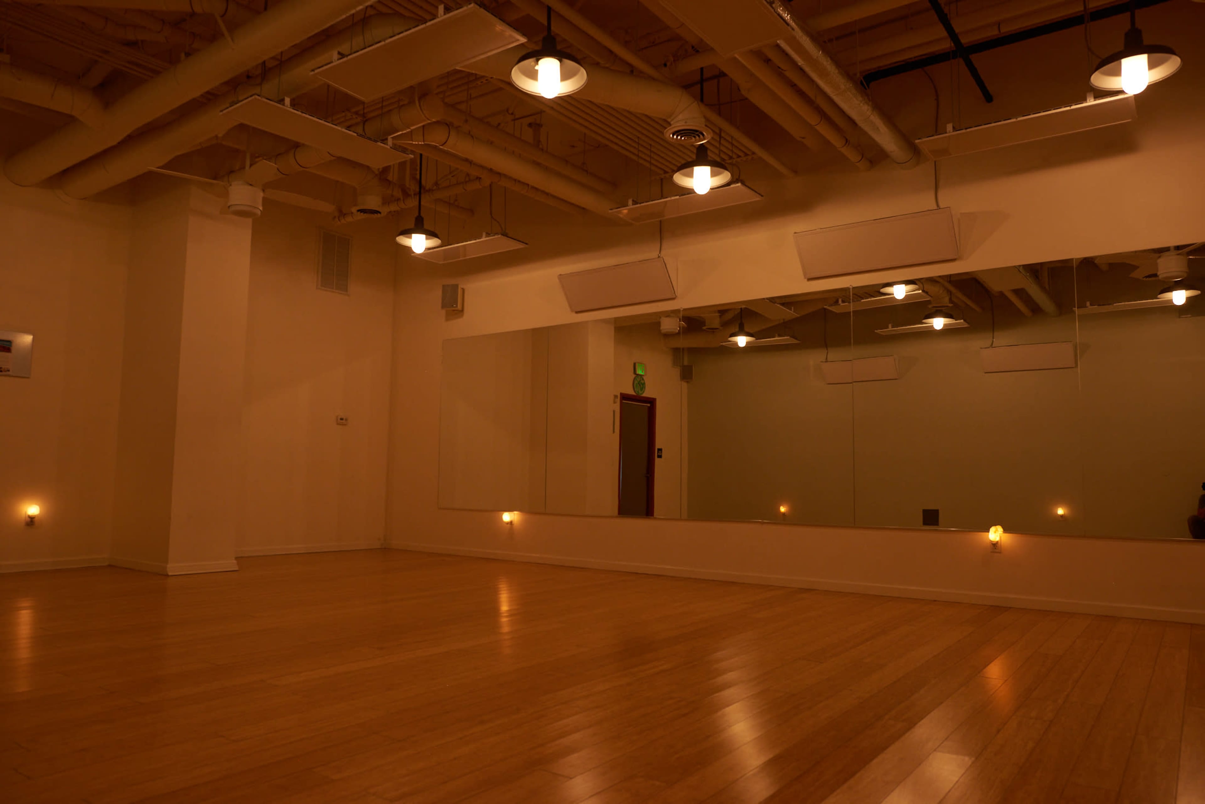 A well-lit dance studio features a wooden floor and wall mirrors, with several overhead lights illuminating the space.