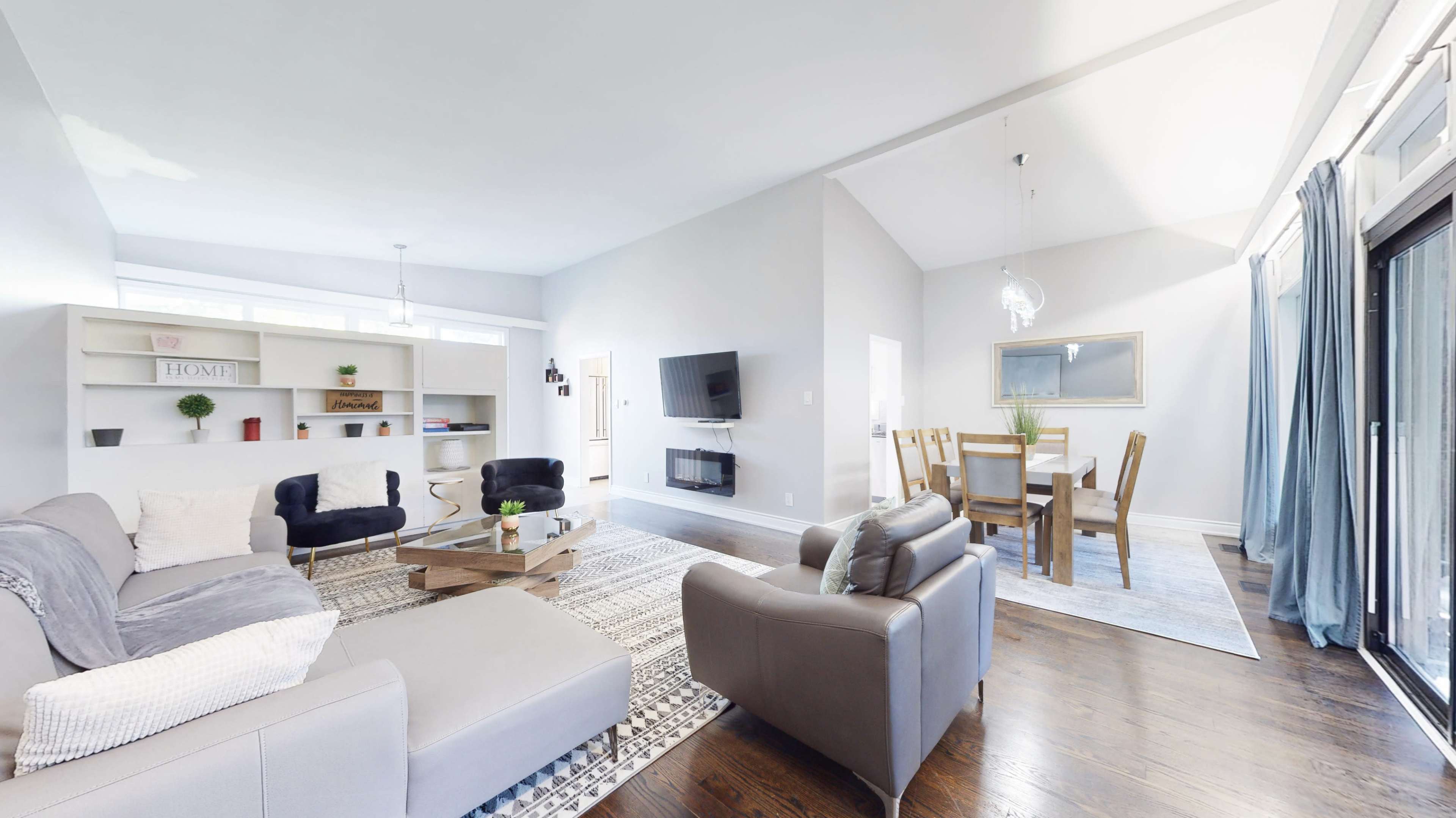 The image shows a spacious living room with modern furniture, a dining area, and large windows that allow natural light to enter.
