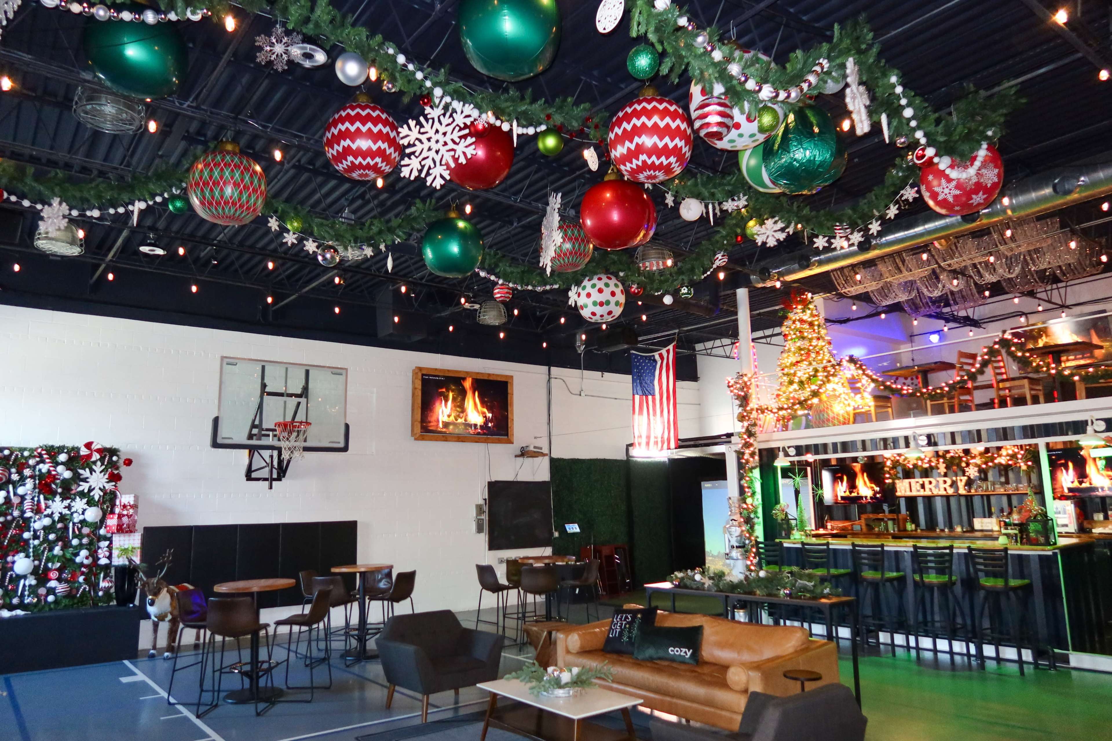 The image depicts a festive indoor space decorated for the holidays, featuring large ornaments hanging from the ceiling, a Christmas tree, and a basketball hoop in one corner.