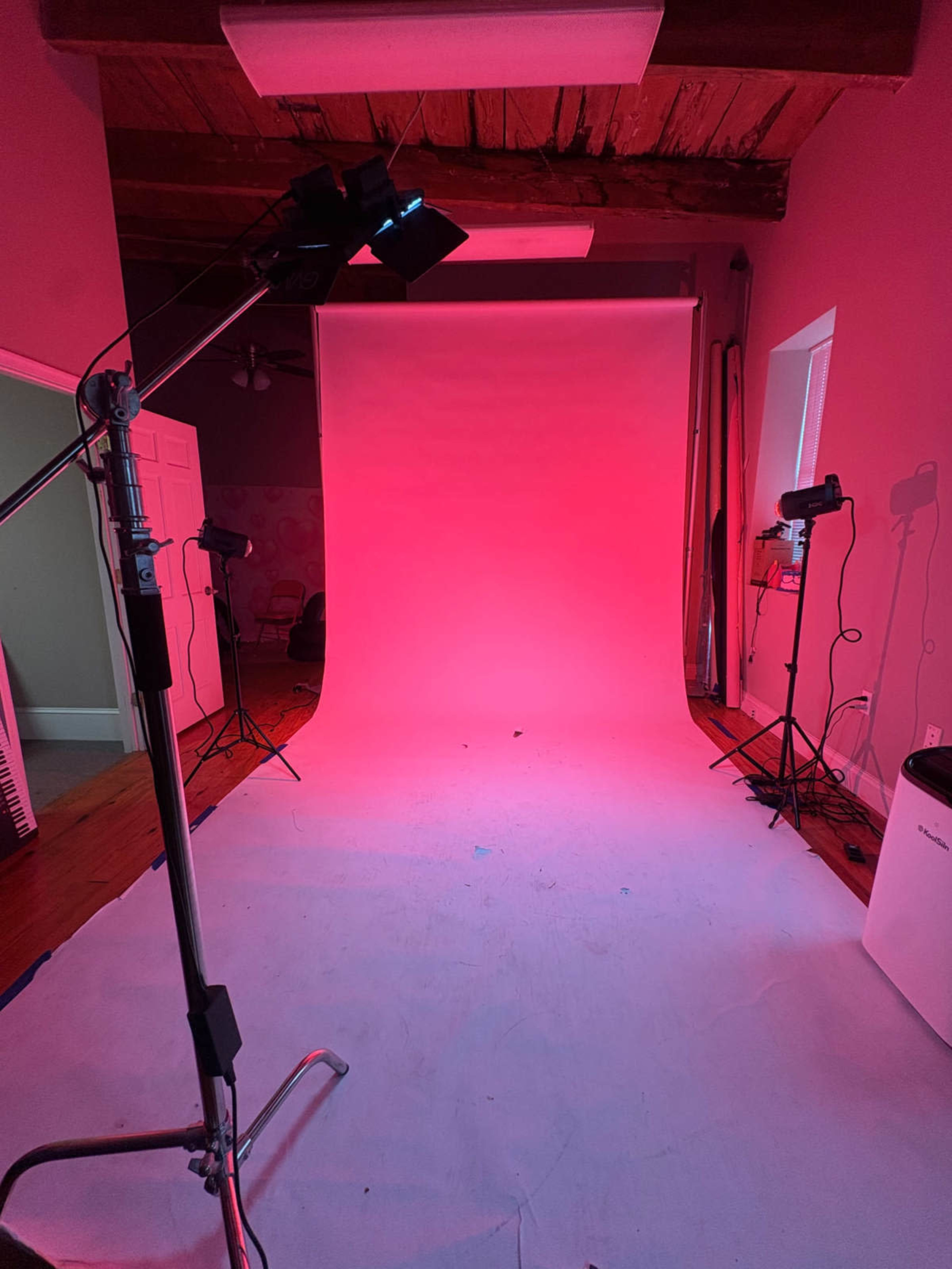 The image shows a photography studio with a pink backdrop, illuminated by multiple lighting fixtures.