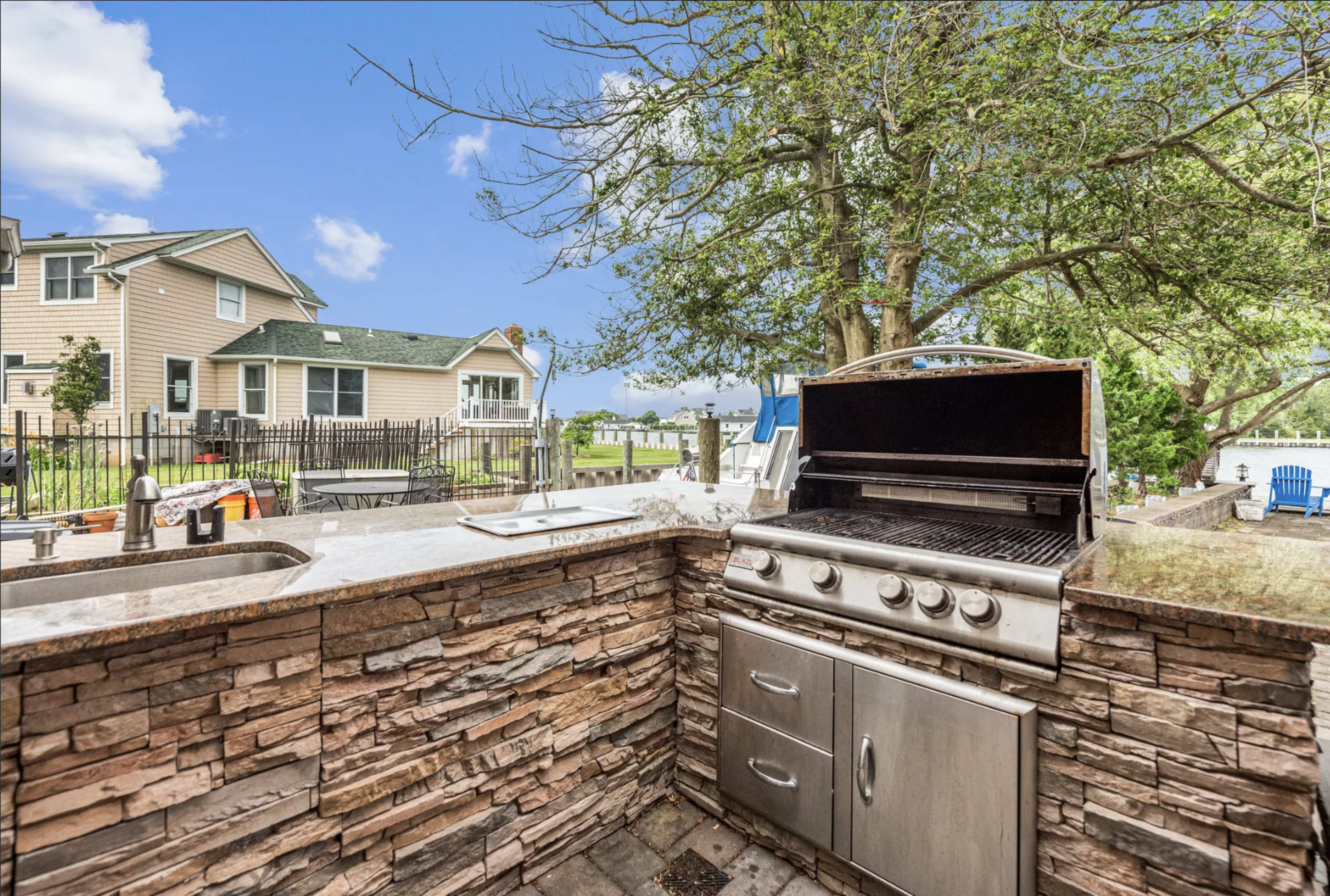 An outdoor kitchen area featuring a stone barbecue grill, with a view of a backyard and houses in the background.