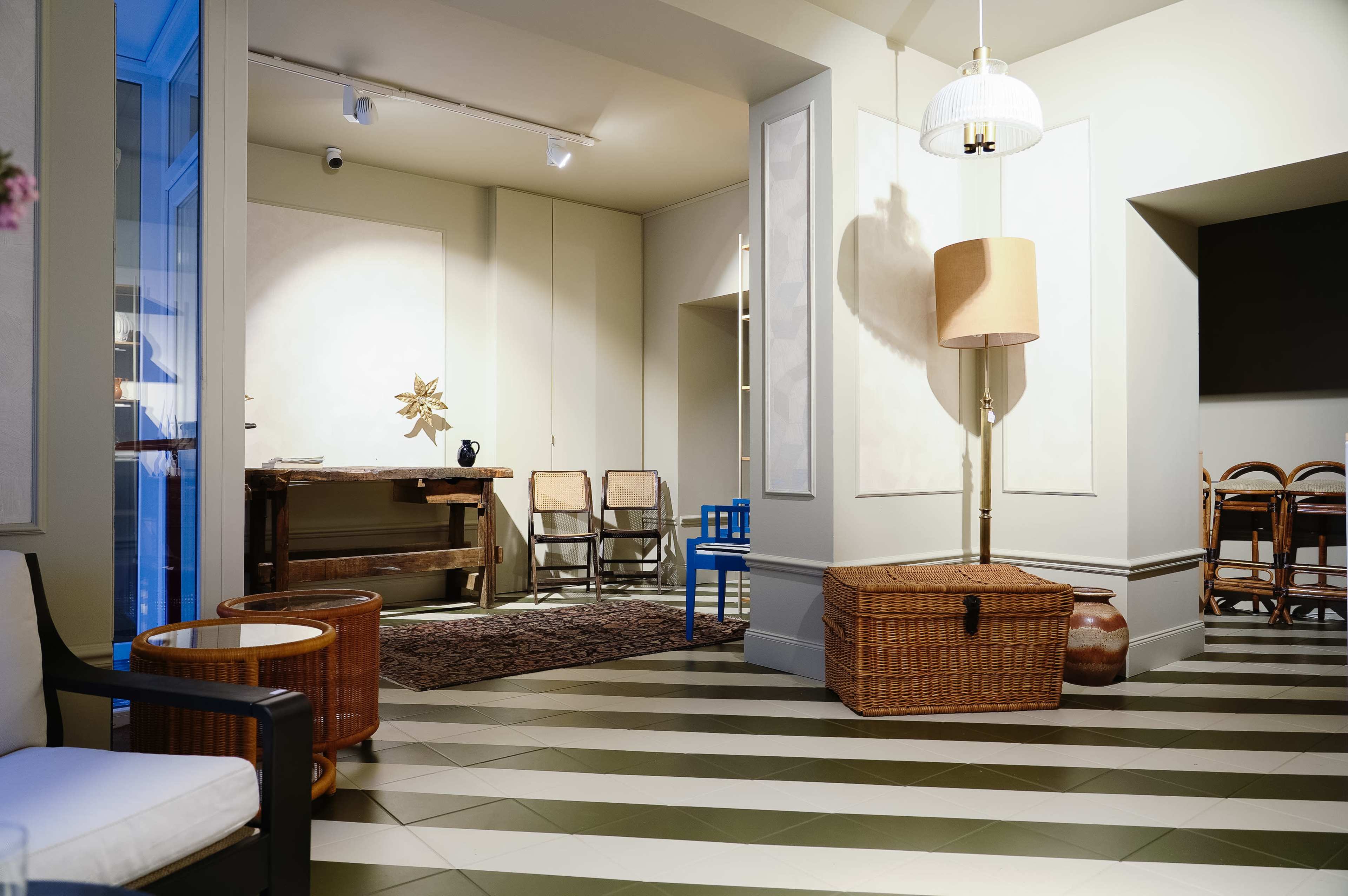 The image shows a modern interior space featuring a patterned floor, a wooden table, chairs, a lamp, and decorative items.