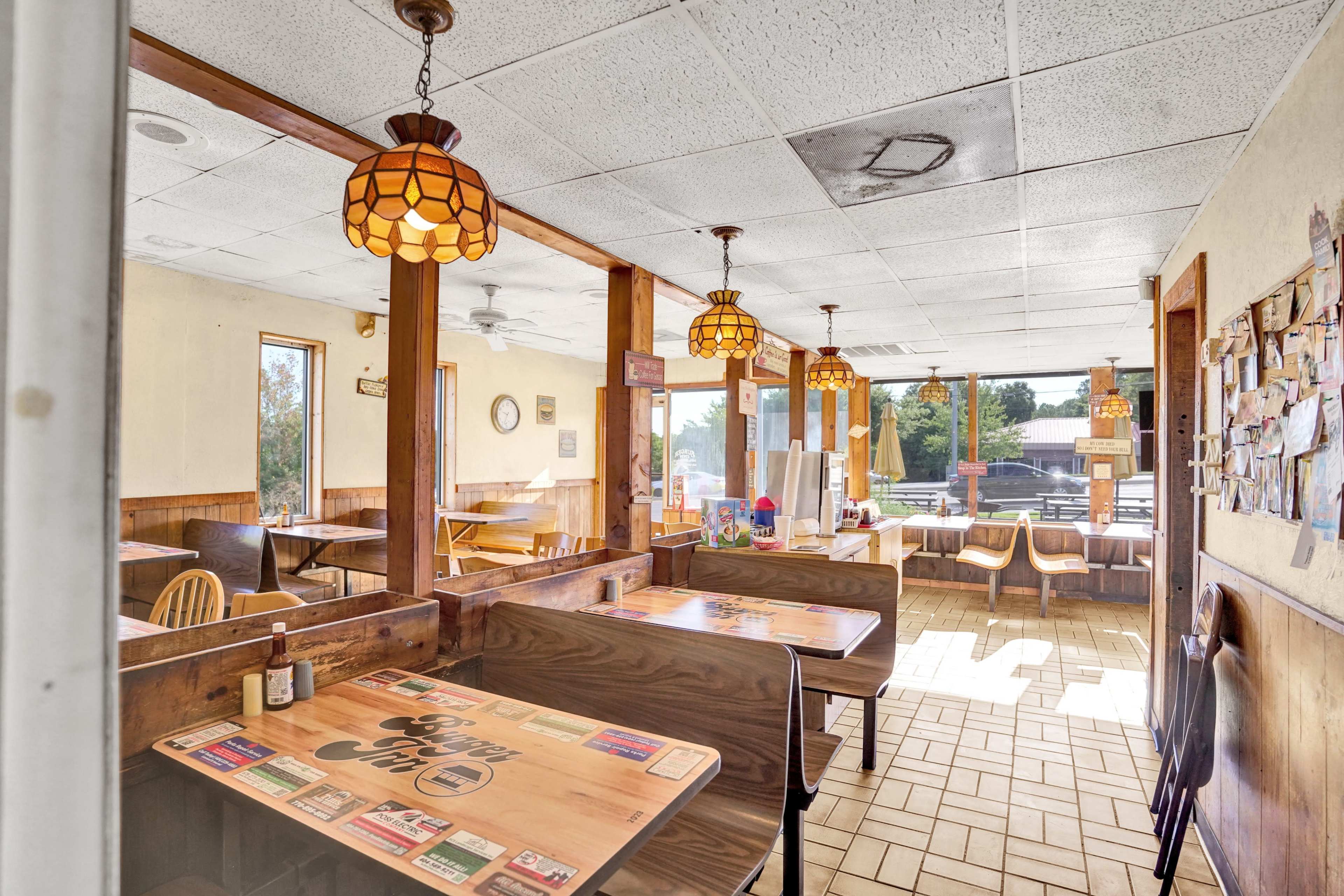 The image shows the interior of a casual dining restaurant with wooden booths and tables, featuring vintage hanging lamps and a collection of photos on the walls.