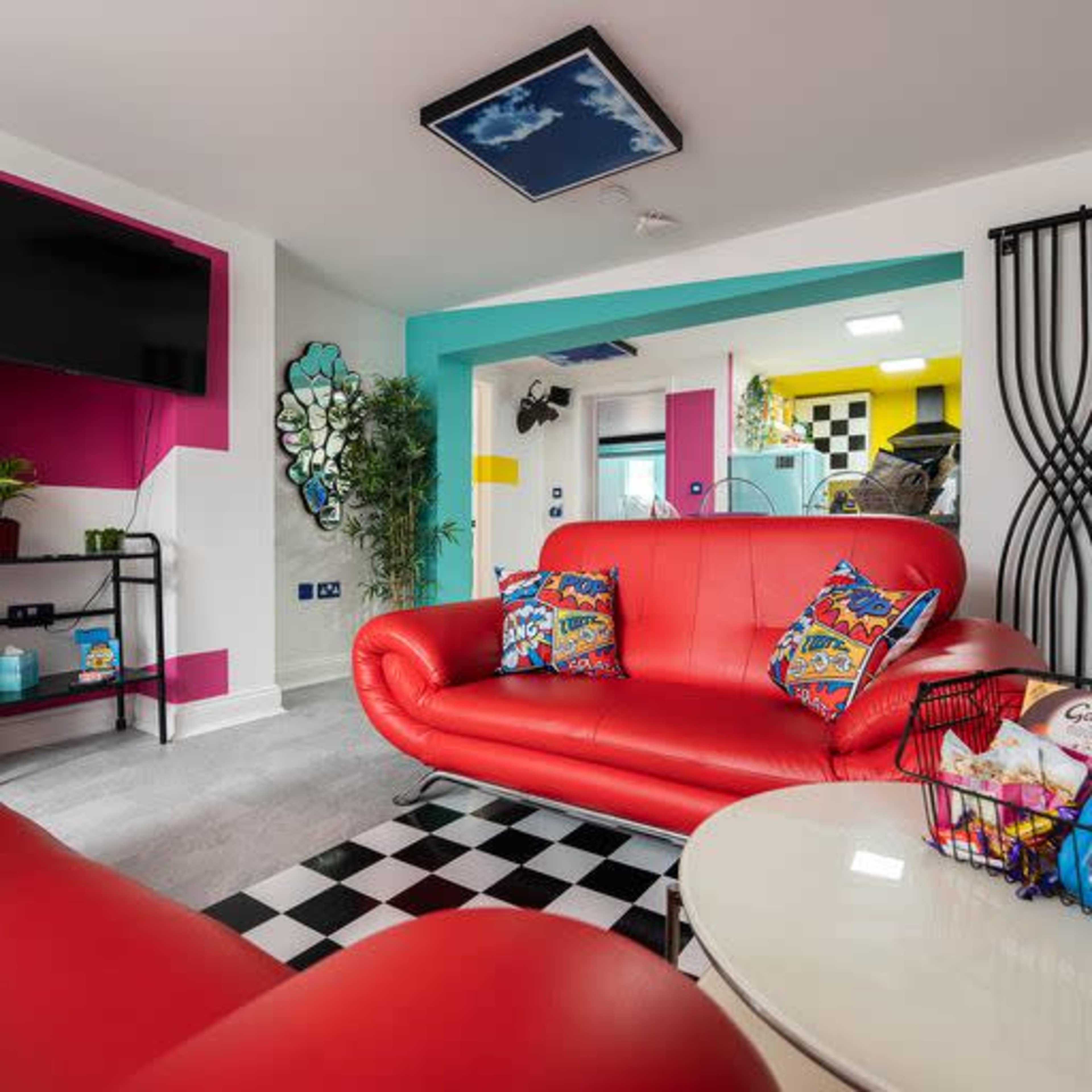 A modern living room features a red sofa, black-and-white checkered flooring, a large television, and colorful wall accents.