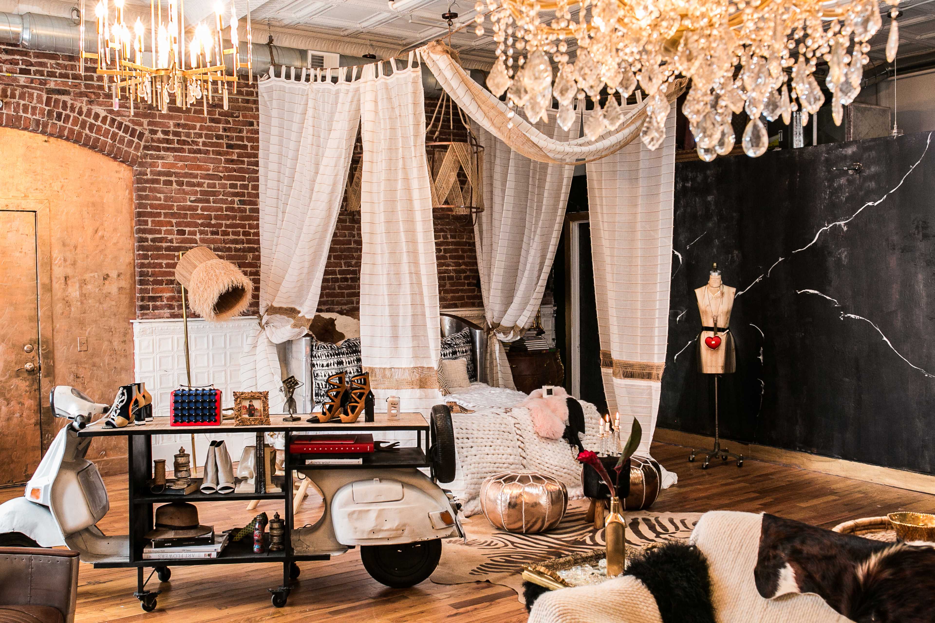 A stylish interior space featuring a vintage scooter, draped fabrics, and various decorative items arranged amid exposed brick walls and elegant lighting.