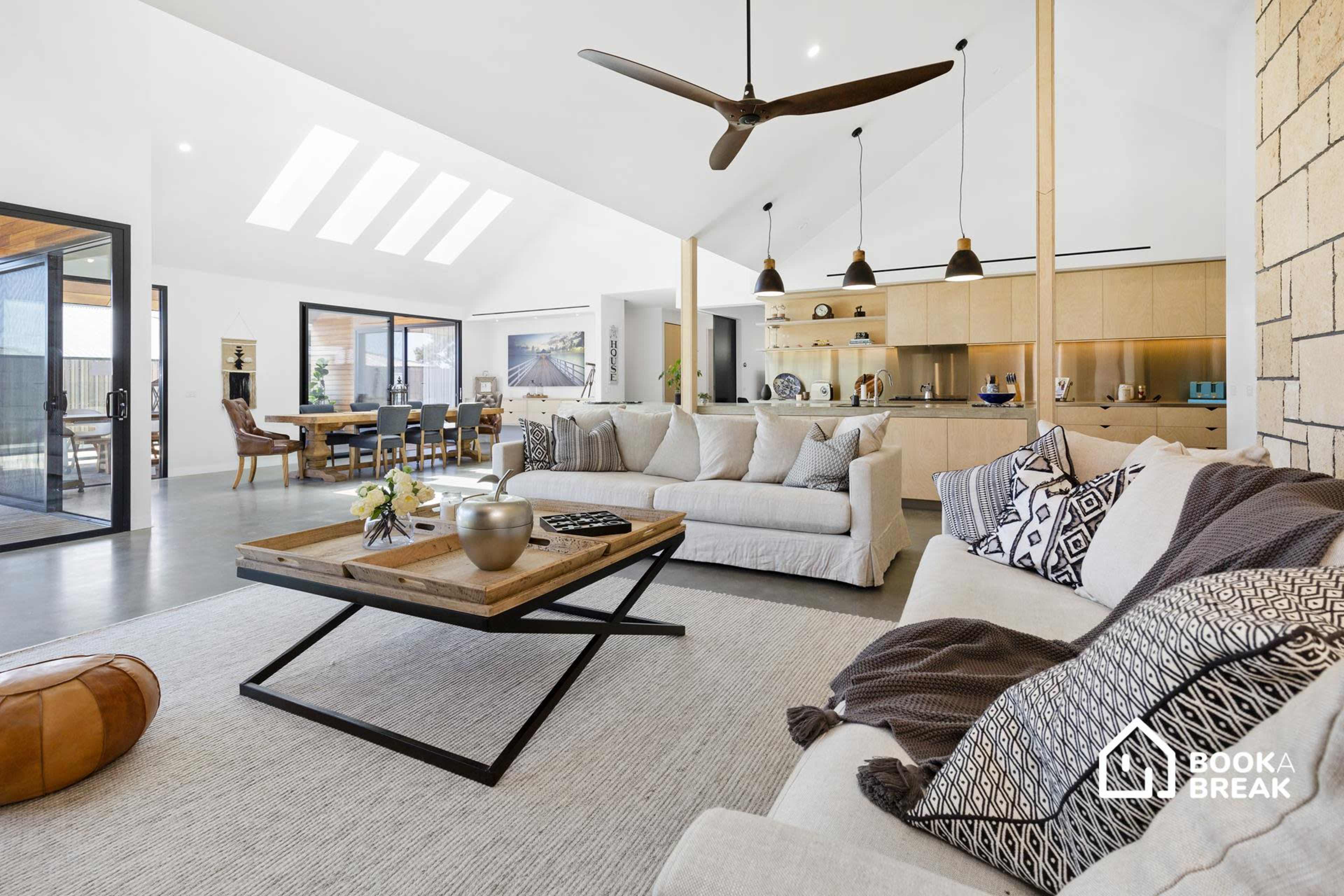 A modern living room with a light-colored sectional sofa, a wooden coffee table, and an open layout that connects to a dining area and kitchen.