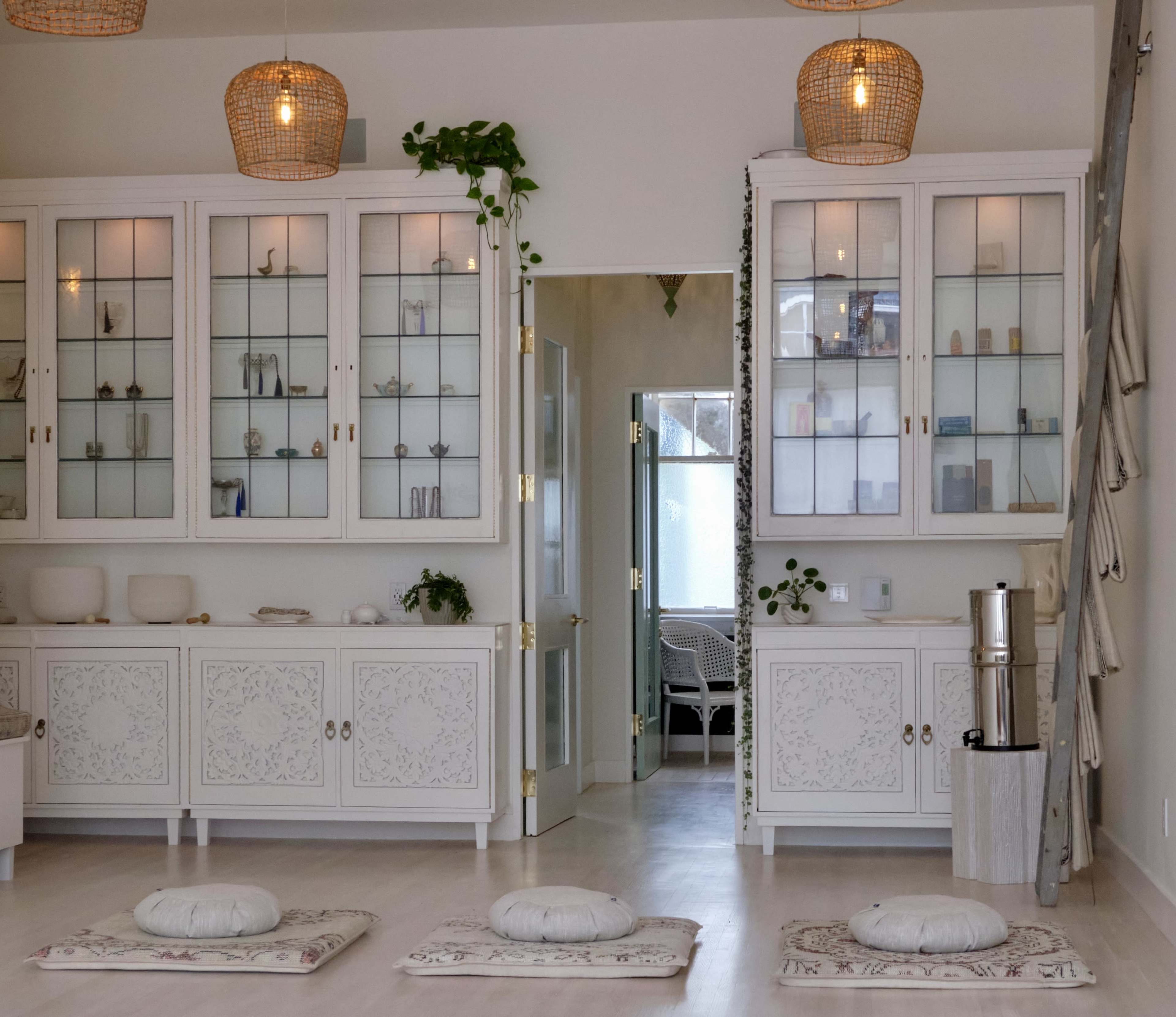 A well-organized and light-filled room features glass-fronted cabinets displaying decorative items, with cushions placed on the floor for seating.