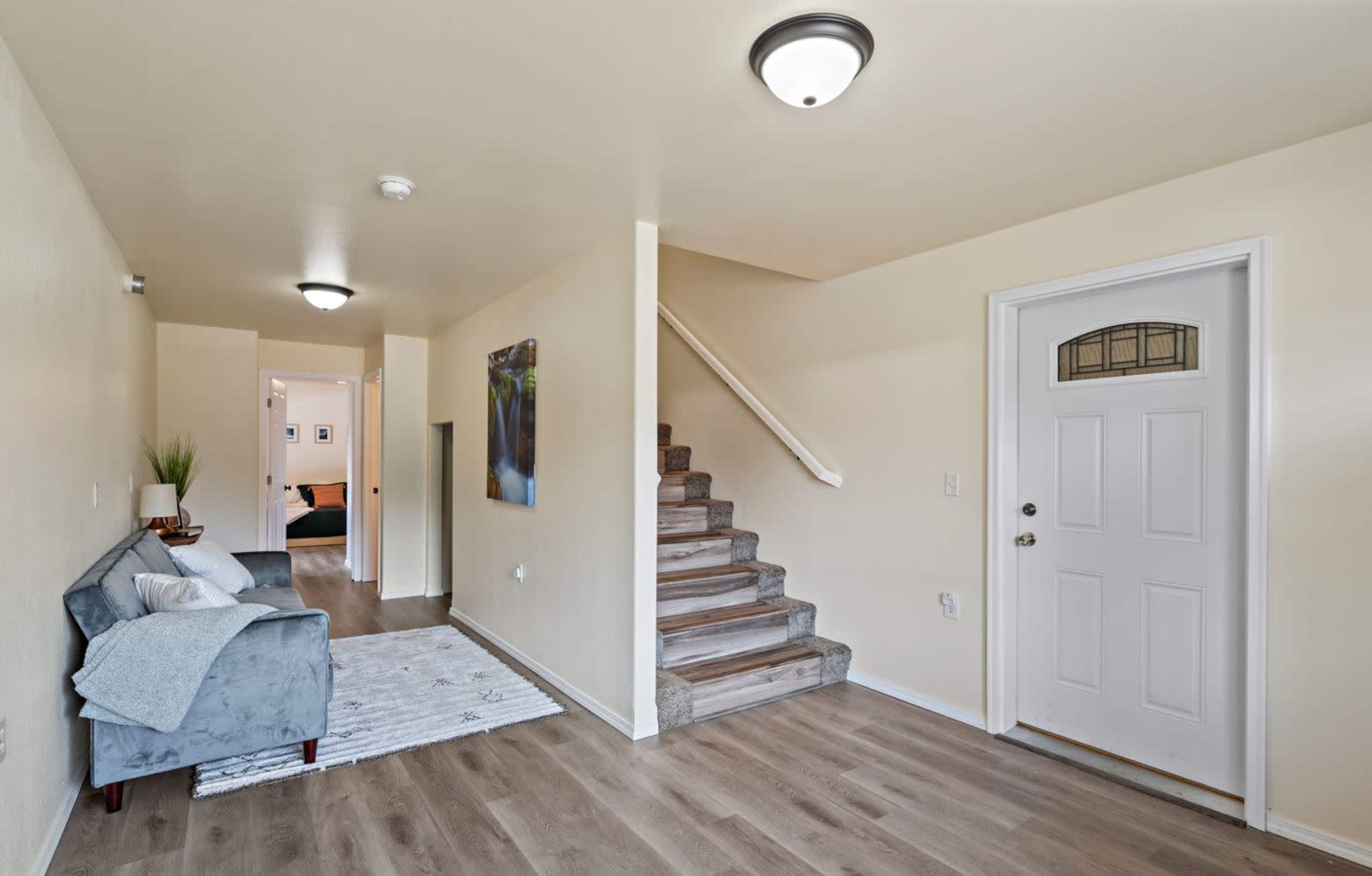 A foyer with a staircase leading up, a small couch, and a door on the right.