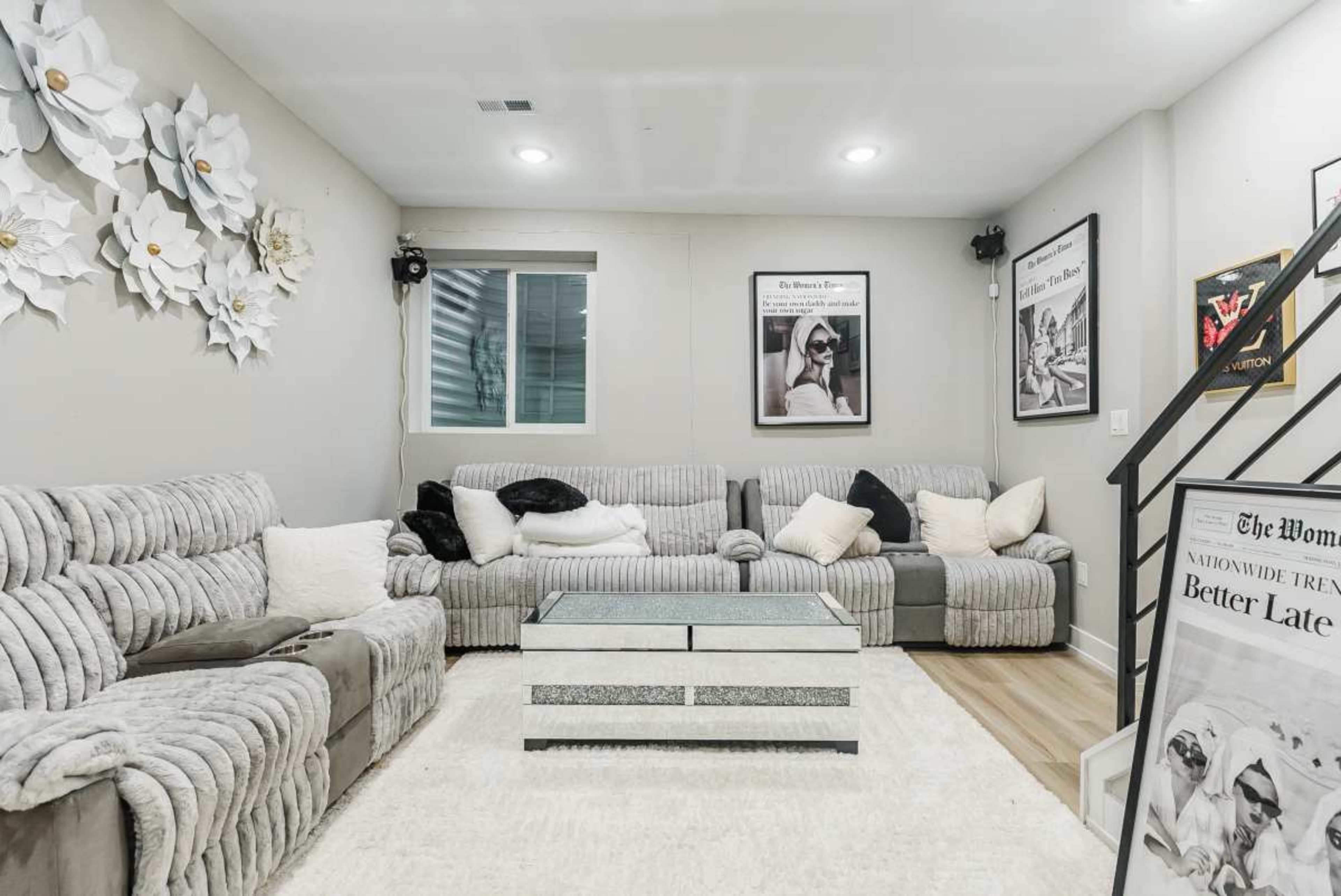 The image depicts a cozy living room with a sectional sofa arranged around a coffee table, decorative wall art, and a textured area rug.
