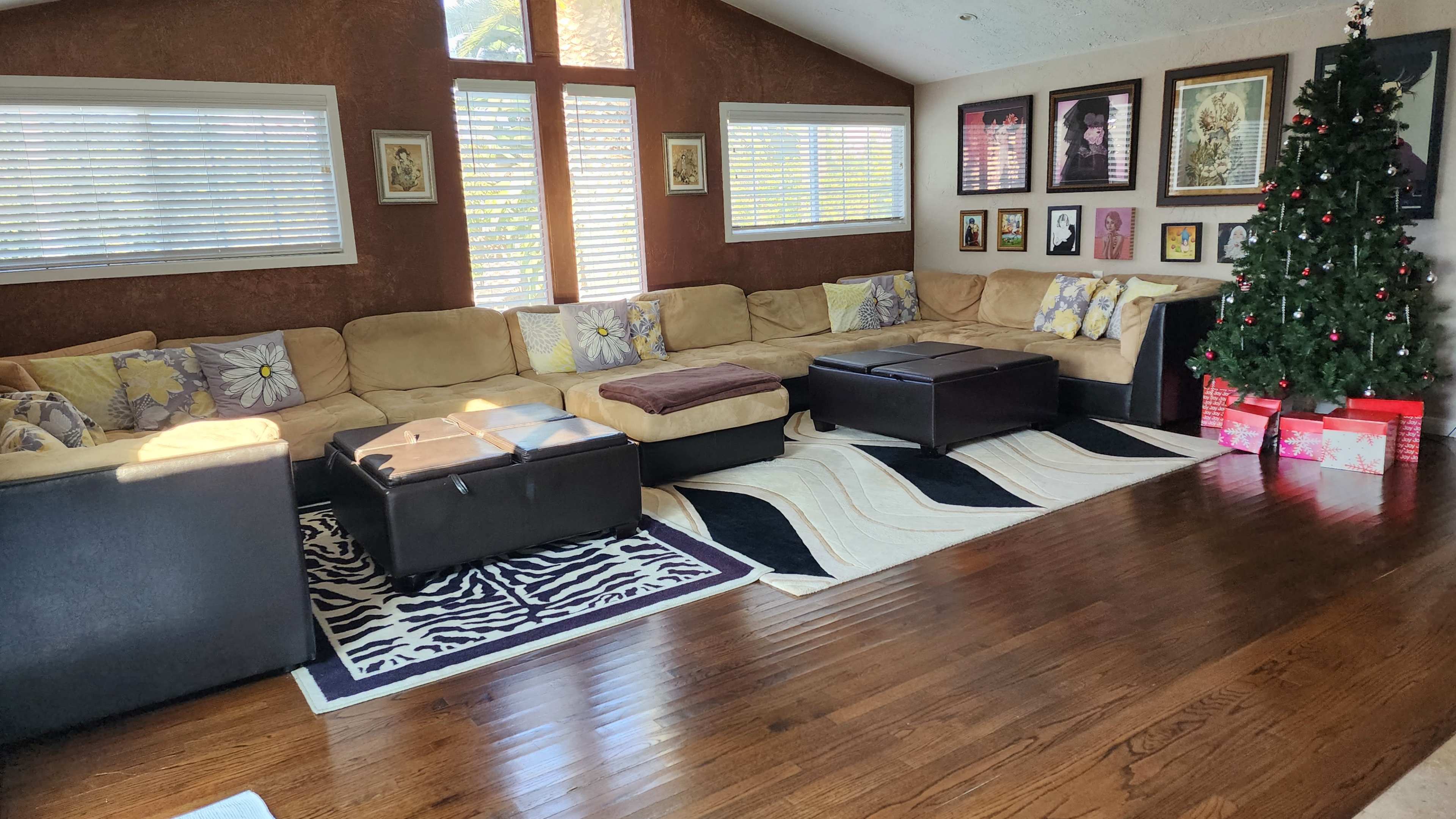 The image shows a spacious living room with a large sectional sofa, a decorative area rug, and a Christmas tree adorned with lights and ornaments.