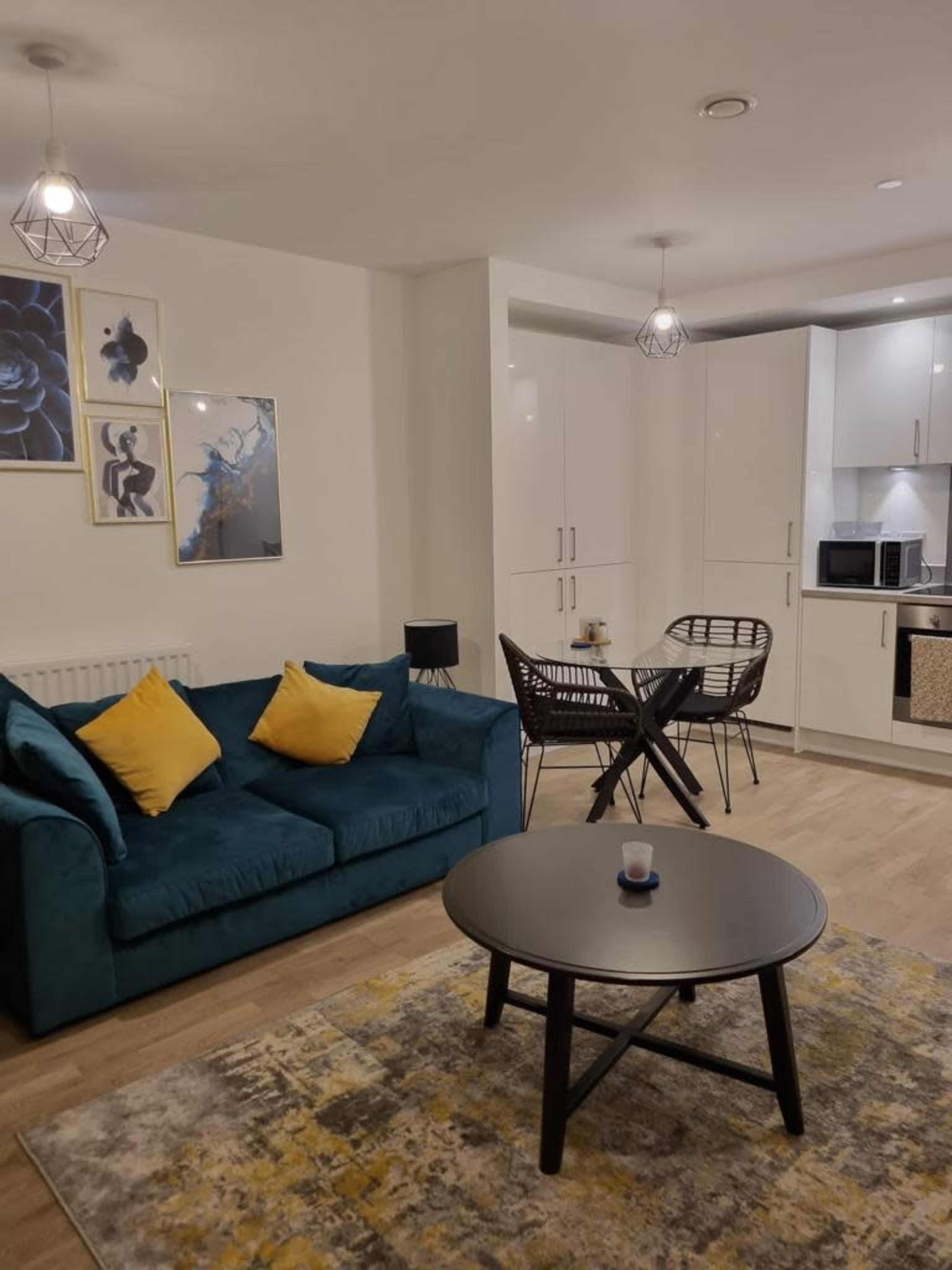 The image shows a modern living room with a teal sofa, a round black table, and a patterned rug, complemented by wall art and pendant lighting.